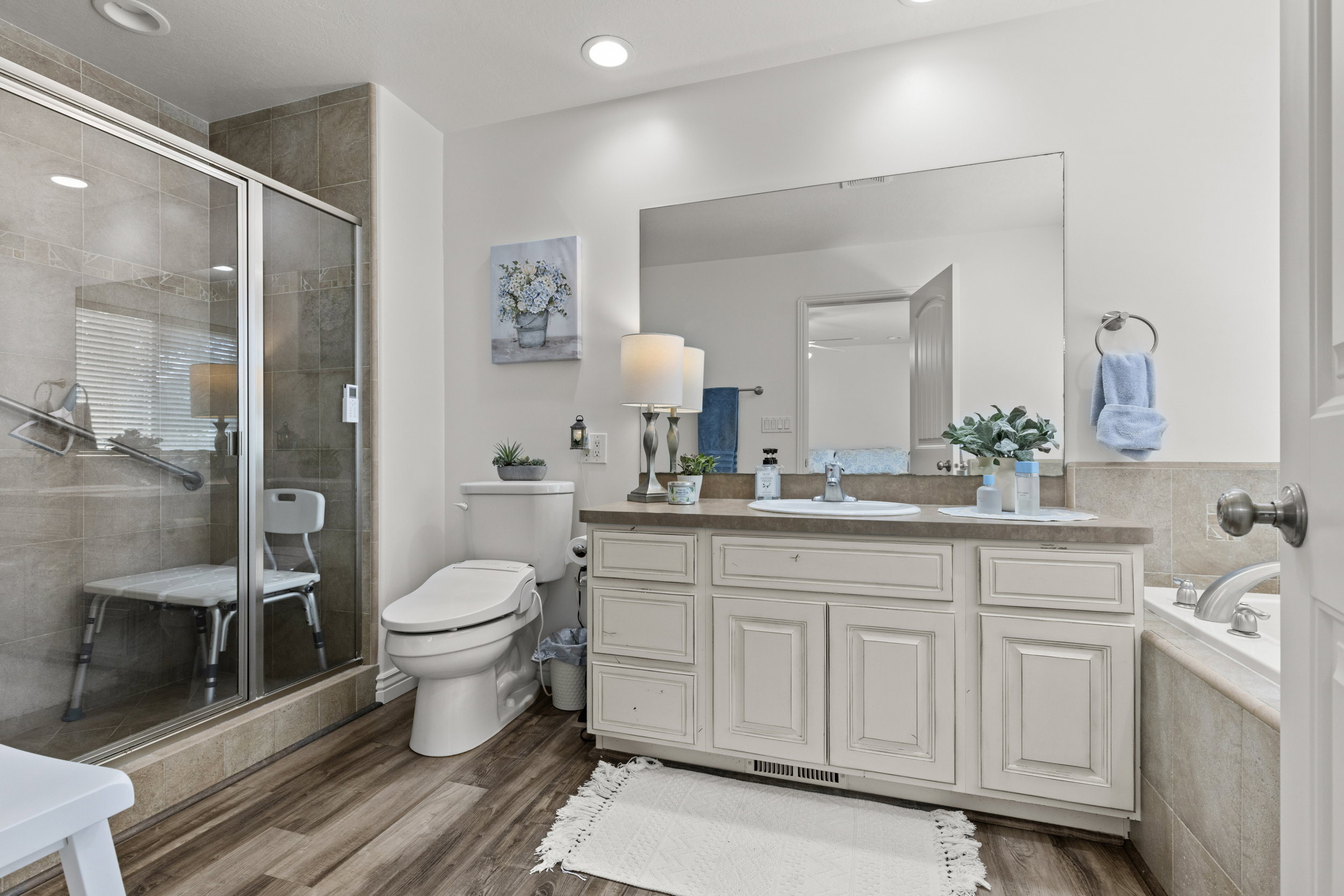 Spacious bathroom featuring wood-finish flooring, a glass-enclosed shower with tiled walls, and a large vanity with a single basin sink and ample storage