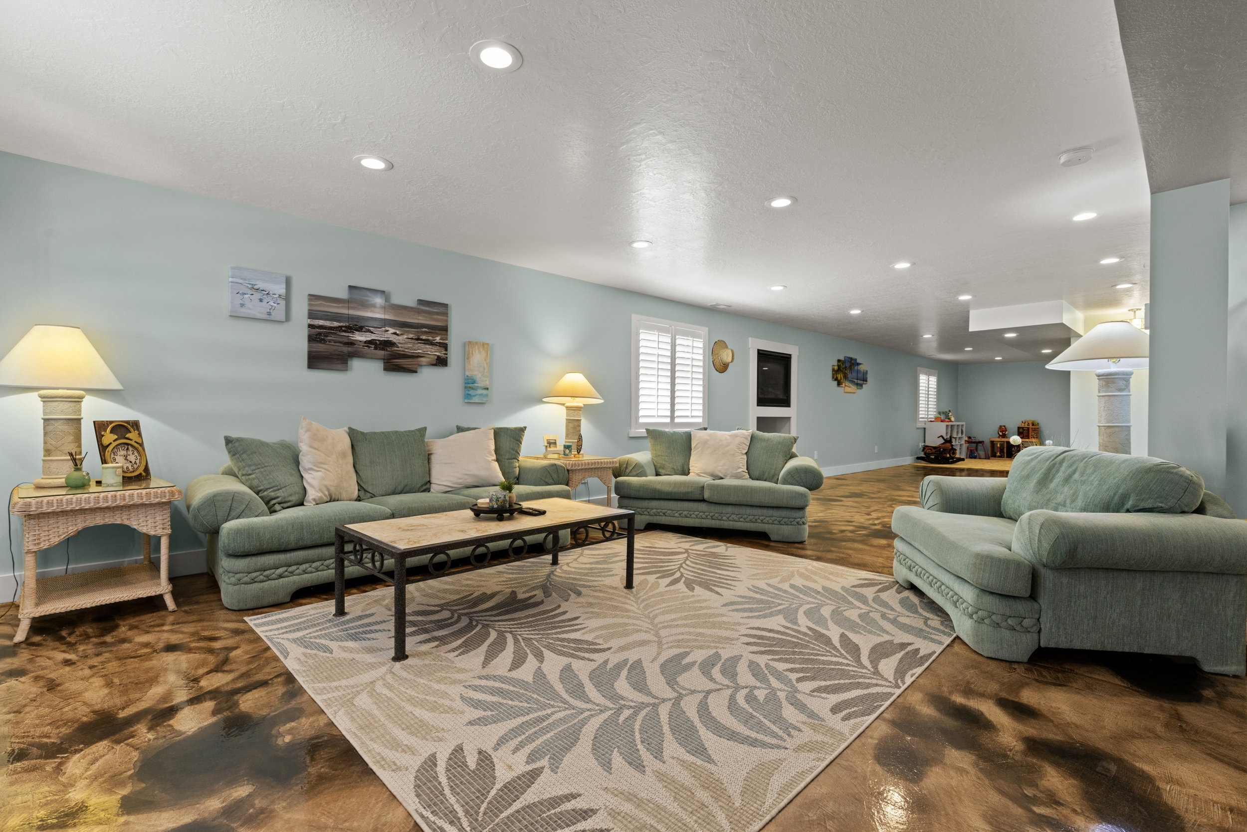 Spacious living area featuring recessed lighting, light blue walls, and a large area rug with a botanical pattern