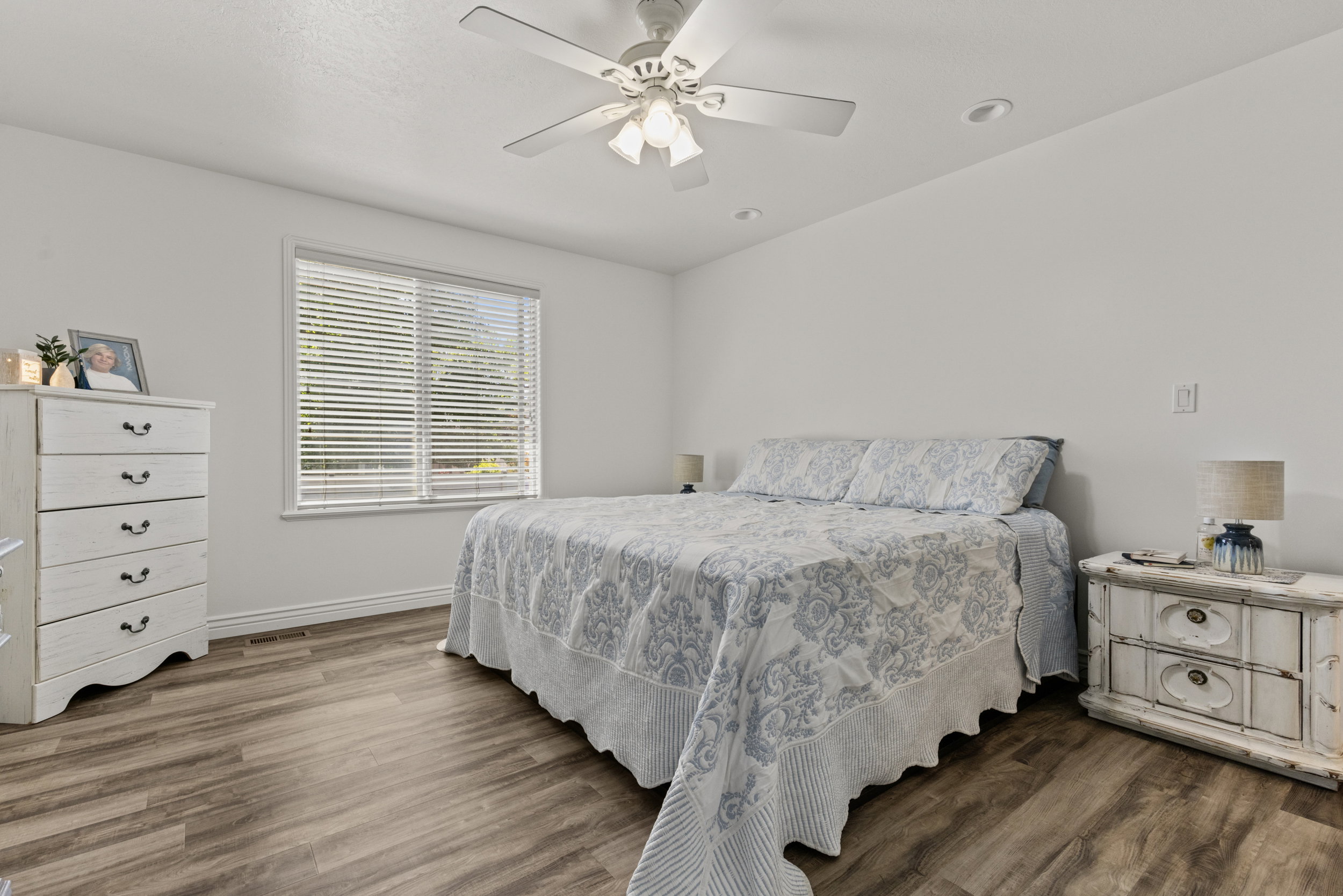 Bright interior space featuring wood-finish flooring, a large window with blinds, a ceiling fan with integrated lighting, and recessed ceiling lights
