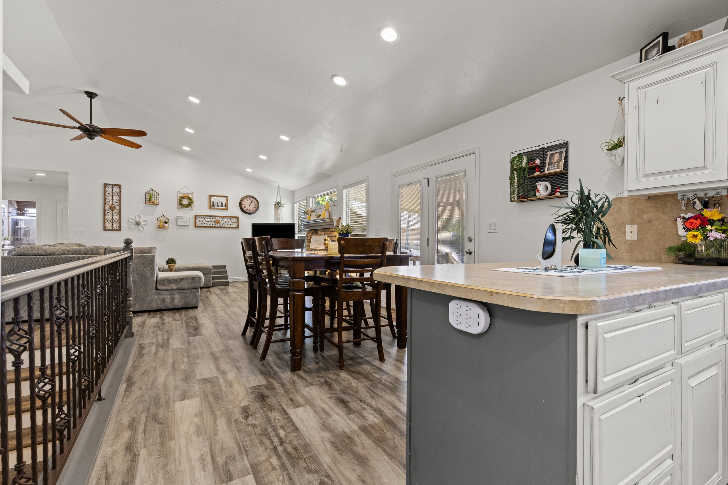 Expansive living area featuring vaulted ceilings with recessed lighting, wood-finish flooring, a kitchen island with a neutral countertop, white cabinetry, and French doors leading to exterior