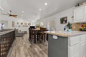 Expansive living area featuring vaulted ceilings with recessed lighting, wood-finish flooring, a kitchen island with a neutral countertop, white cabinetry, and French doors leading to exterior