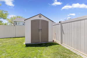 Storage shed with double doors, set within a fenced yard featuring manicured lawn and privacy fencing