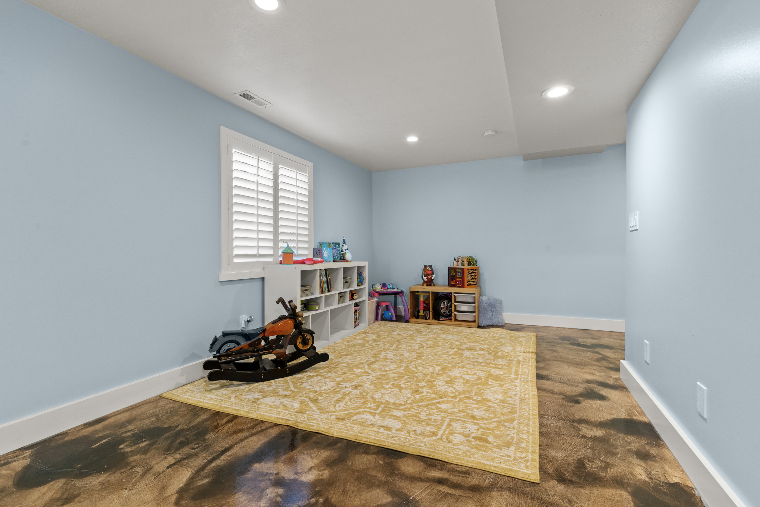 Spacious room featuring light blue walls, white trim, recessed lighting, and a window with white plantation shutters