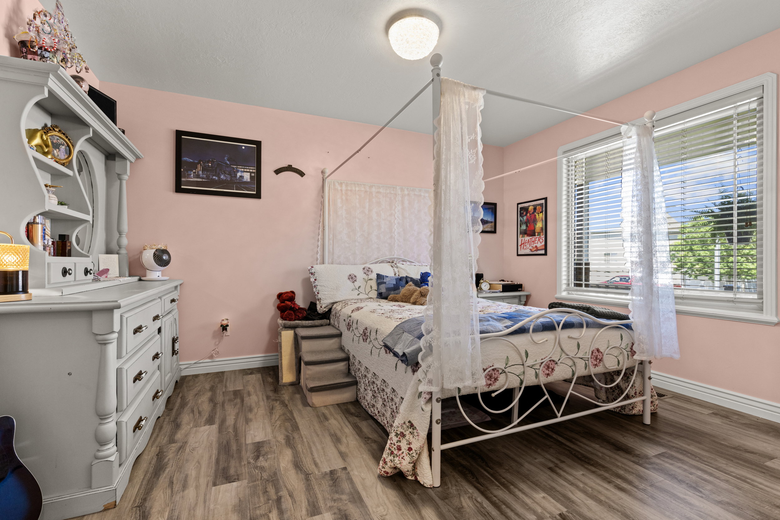 Bedroom featuring wood-finish flooring, a contemporary ceiling light fixture, and a large window with white blinds