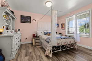 Bedroom featuring wood-finish flooring, a contemporary ceiling light fixture, and a large window with white blinds