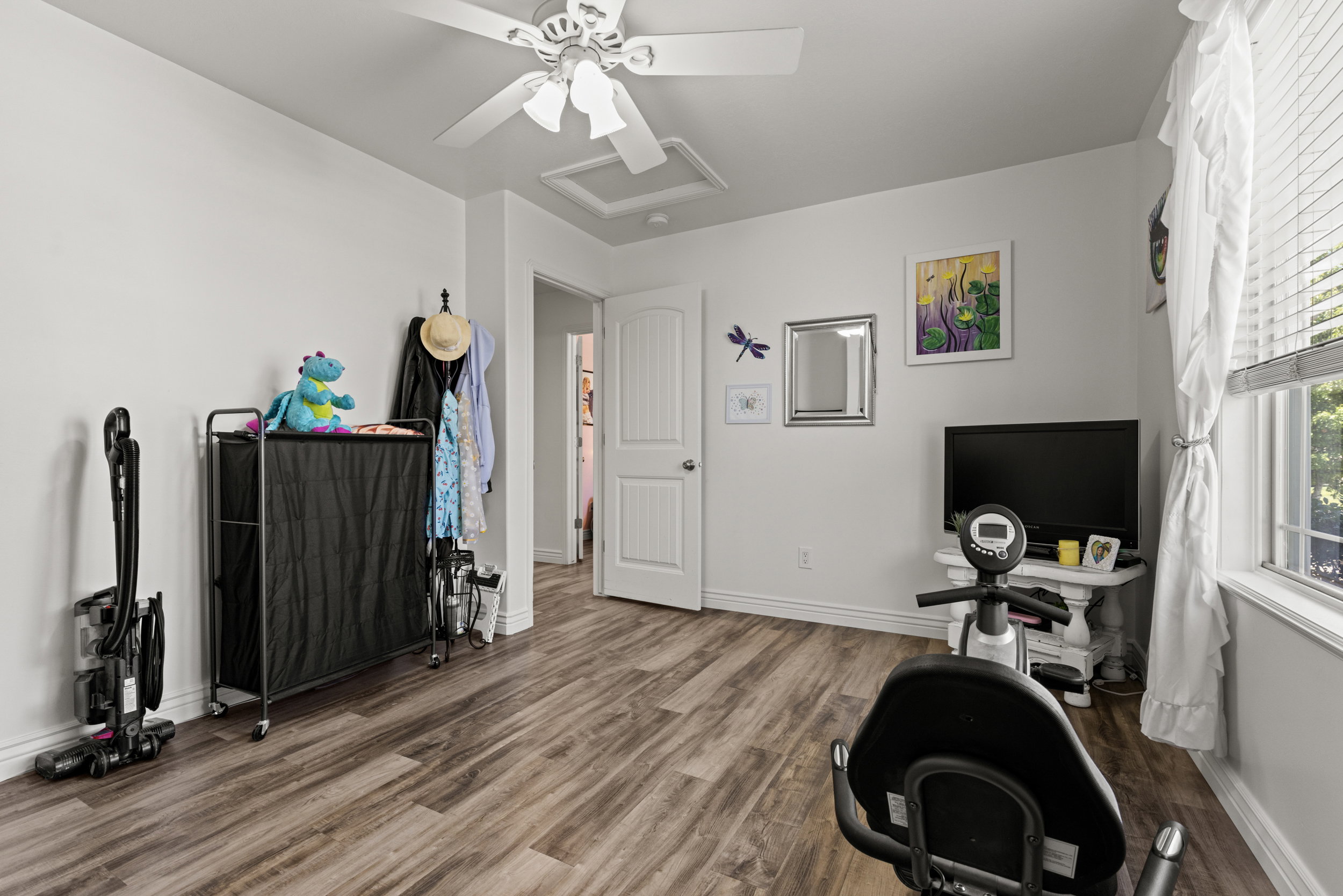 Spacious room featuring wood-finish flooring, white baseboards, and a white ceiling fan