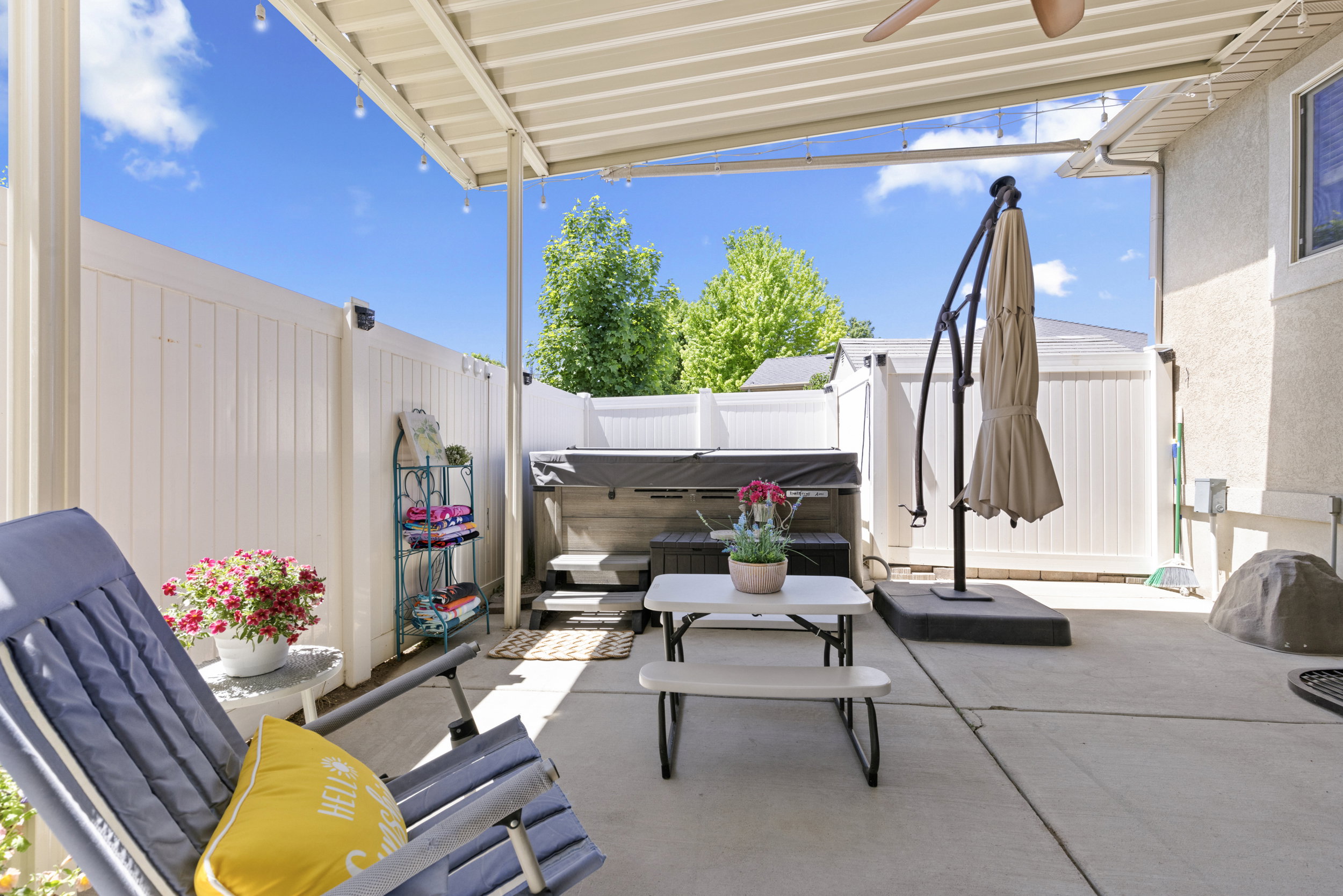 Covered concrete patio featuring a ceiling fan, string lighting, and a built-in hot tub
