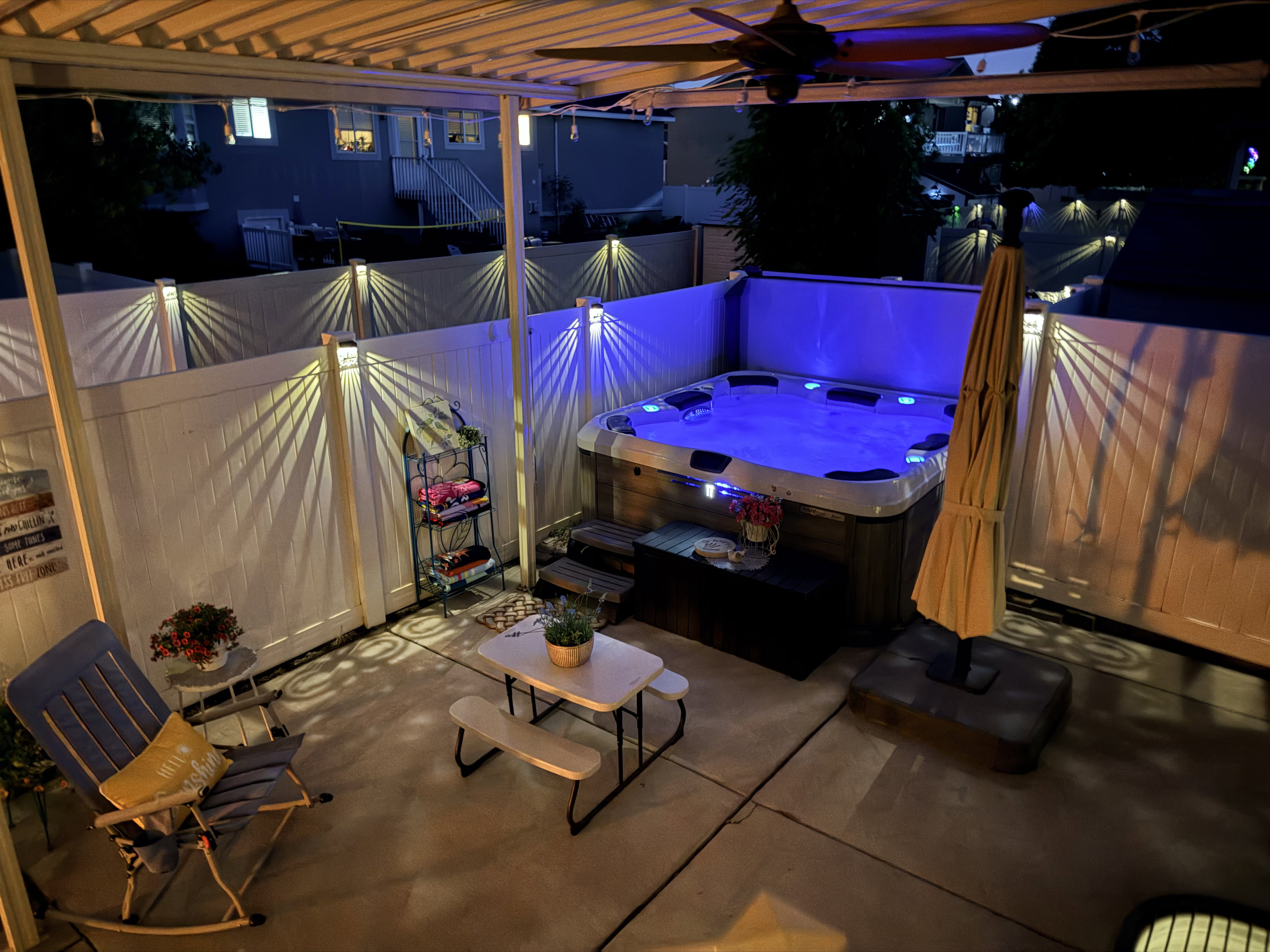 Patio area featuring a built-in hot tub with illuminated water and a coordinating privacy fence