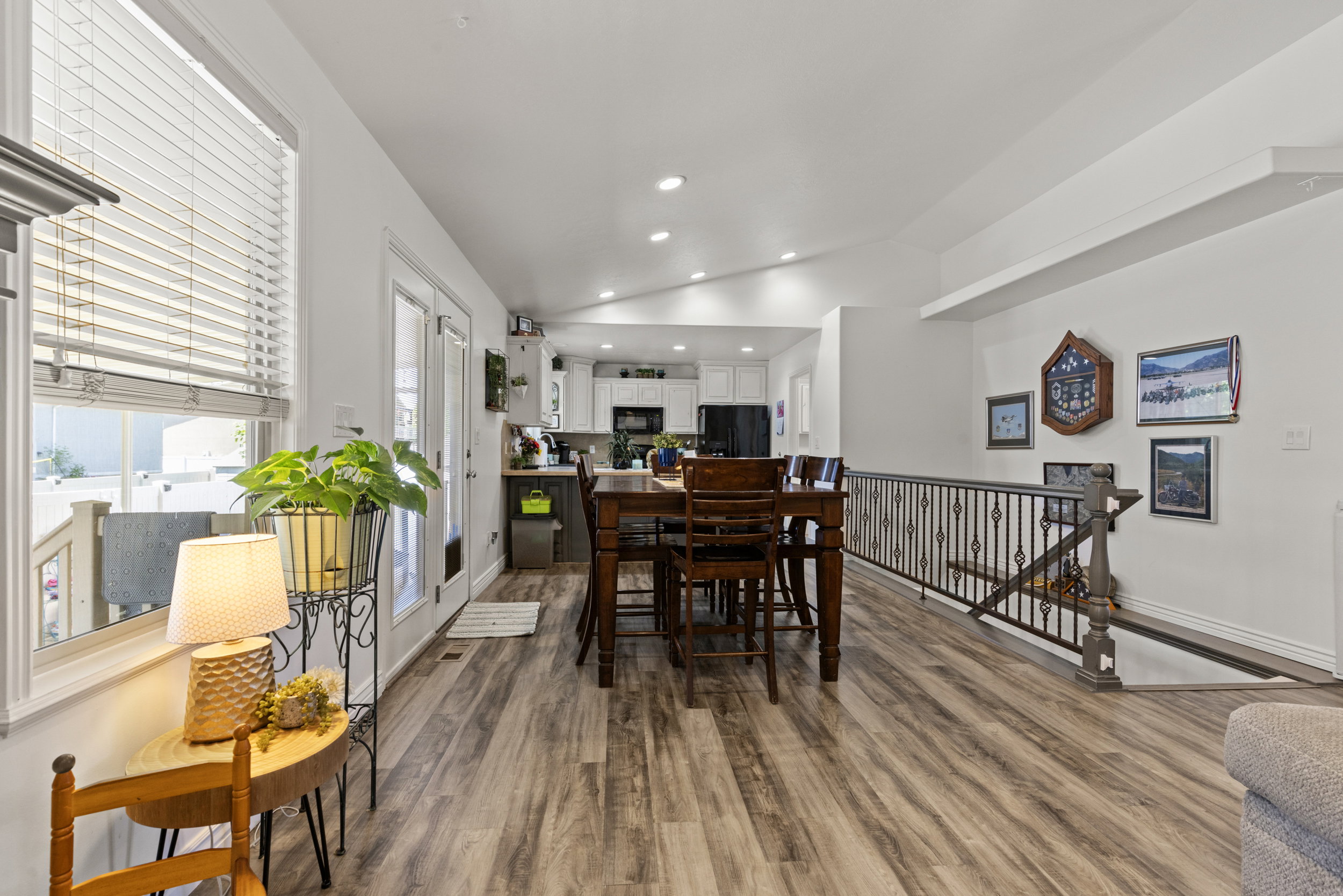 Open-concept living area featuring wood-finish flooring, white walls, and an ornate metal staircase railing