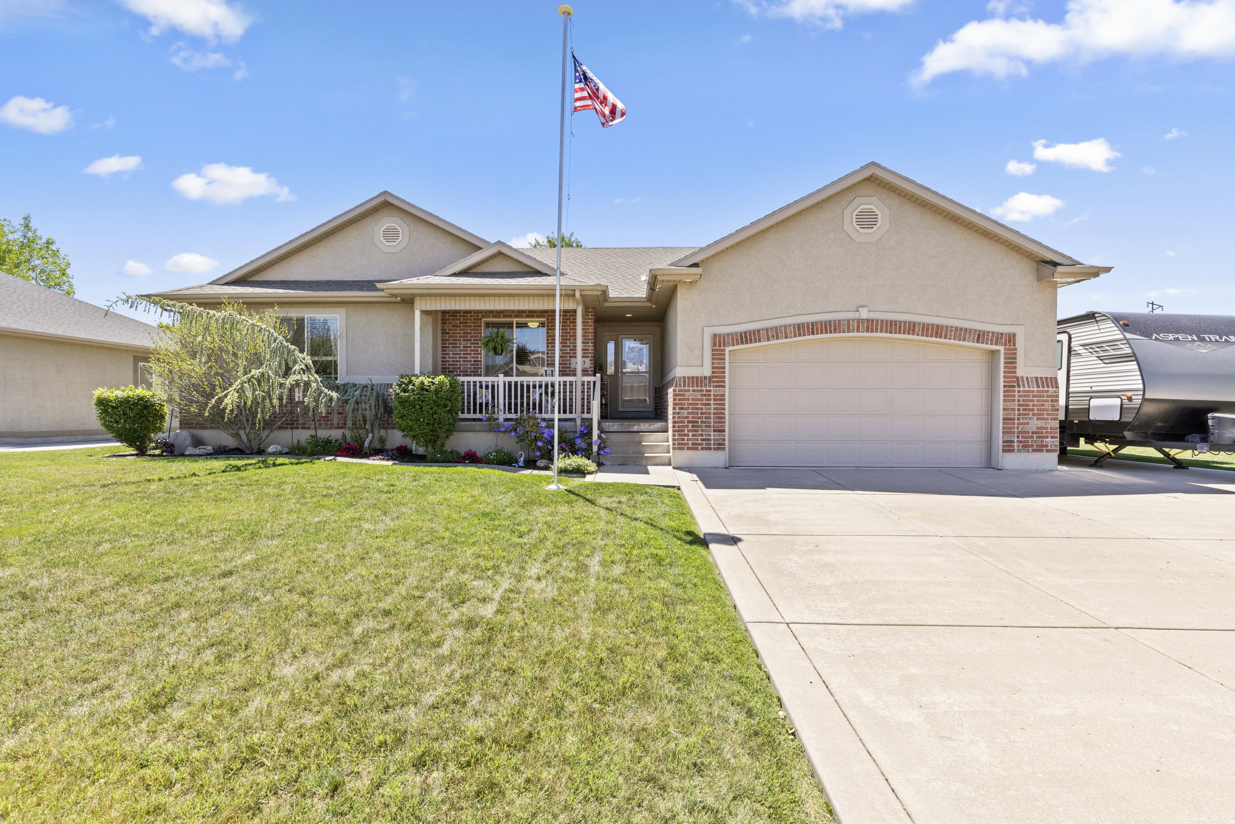 Single-story residence featuring a stucco exterior with brick accents, an attached garage, a covered front porch with white railings, and a concrete driveway