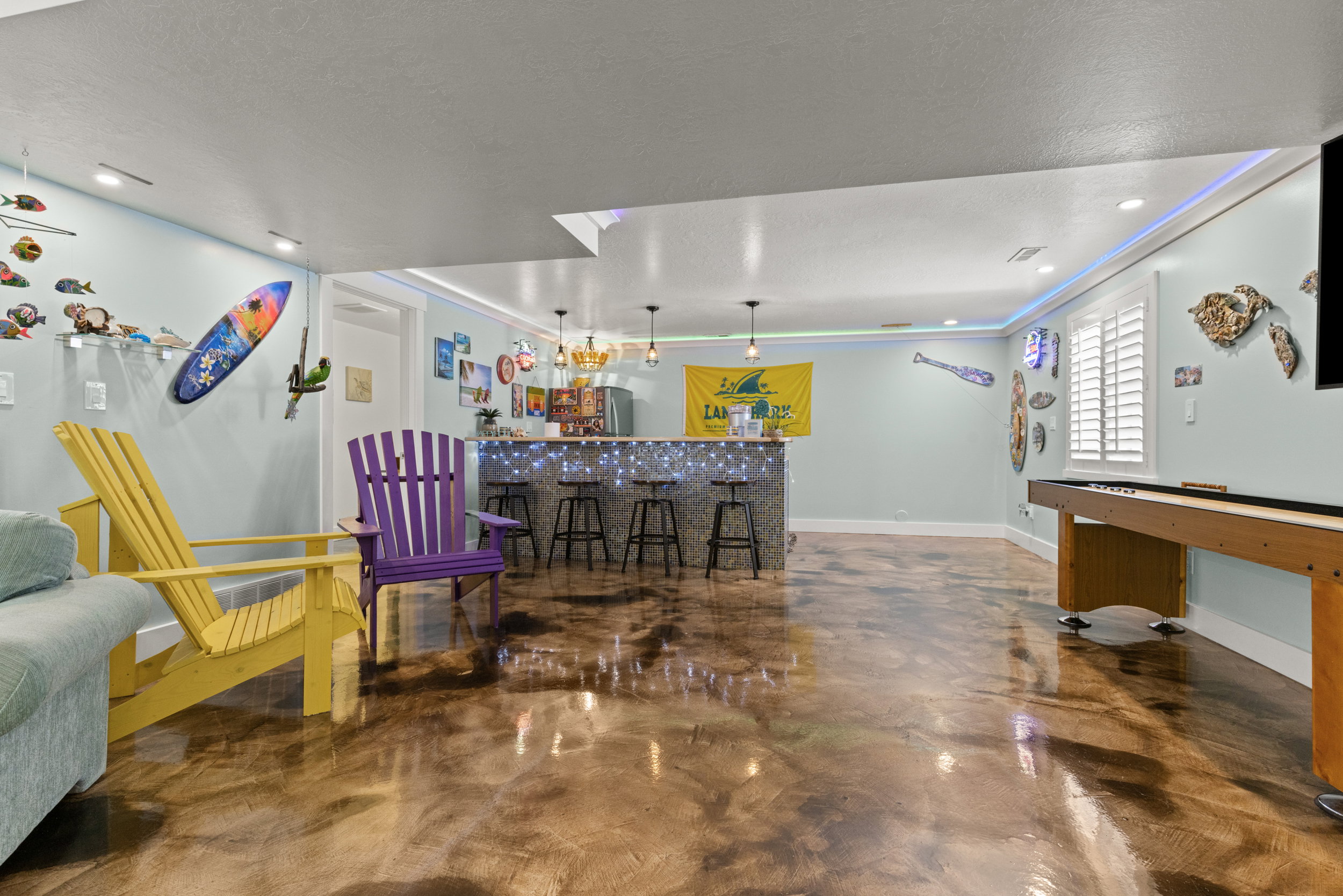 Spacious recreation room featuring polished concrete flooring, a built-in bar with pendant lighting, and recessed ceiling lights
