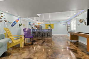 Spacious recreation room featuring polished concrete flooring, a built-in bar with pendant lighting, and recessed ceiling lights