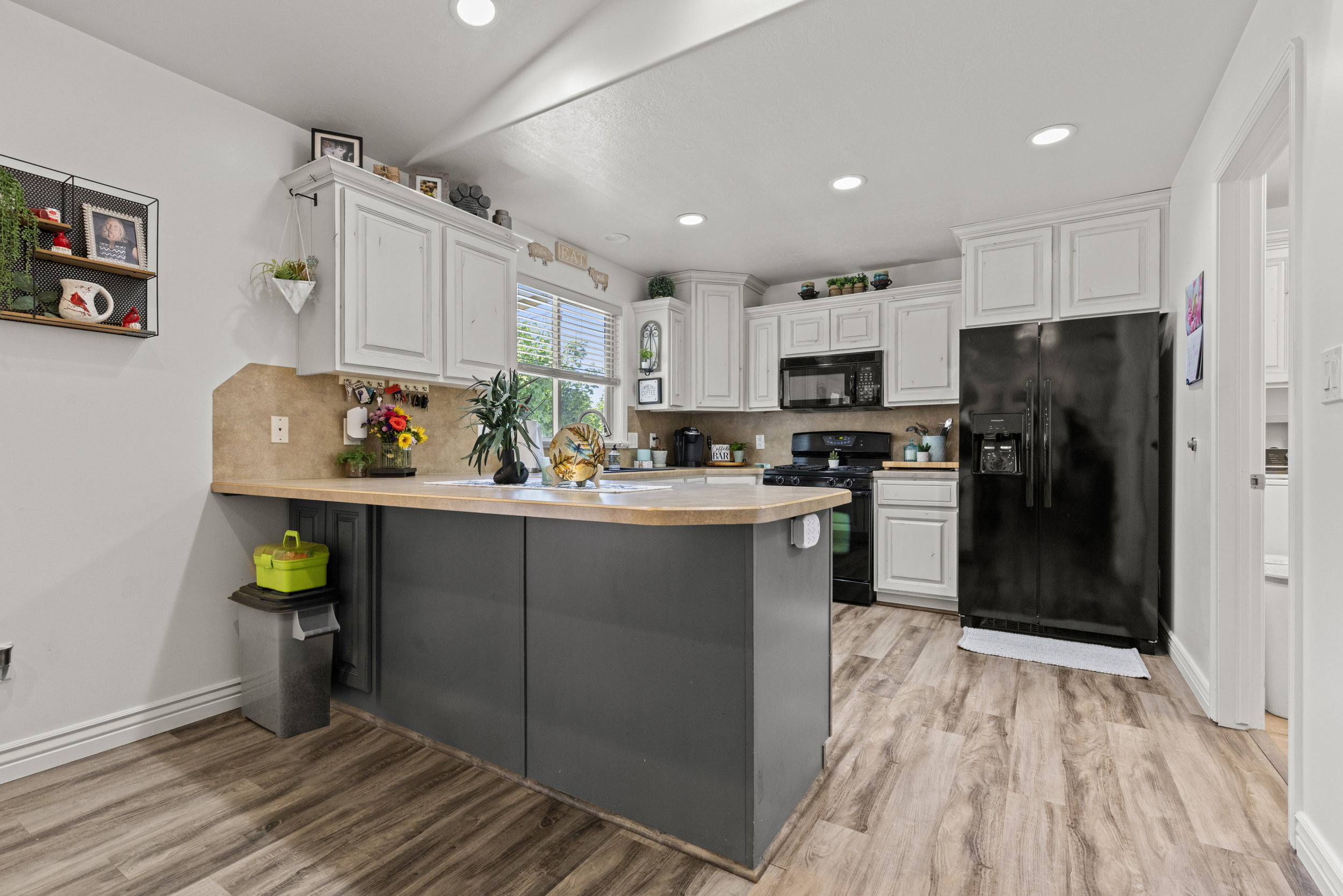 Kitchen featuring white upper cabinetry, dark lower cabinetry, wood-finish flooring, and a window providing natural light