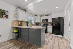 Kitchen featuring white upper cabinetry, dark lower cabinetry, wood-finish flooring, and a window providing natural light