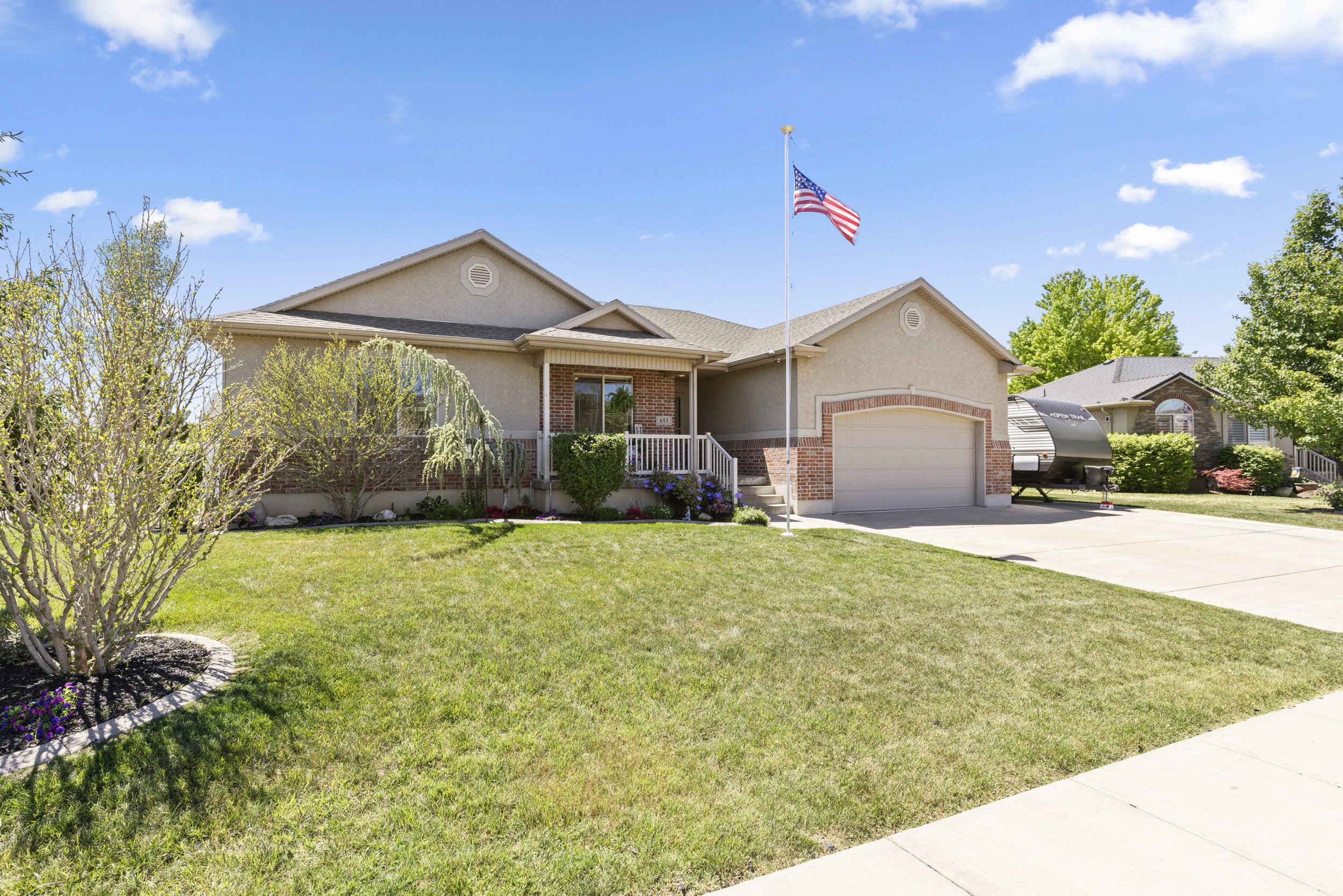 Ranch-style residence featuring a combination of stucco and brick siding, an attached two-car garage, an inviting front porch with white railings, a paved driveway, and a flagpole
