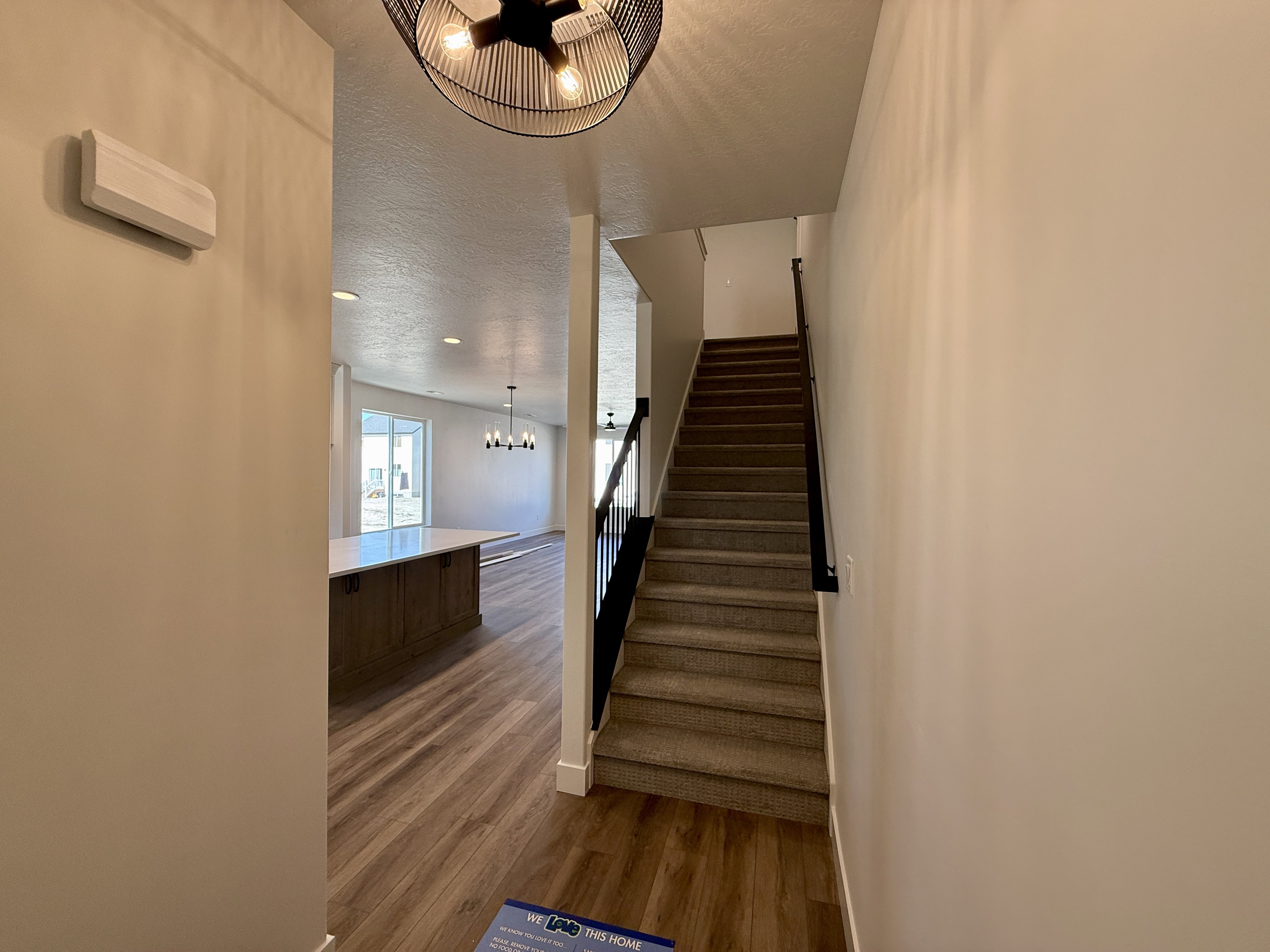 Entryway featuring wood-finish flooring, a contemporary ceiling fixture, and a carpeted staircase with dark railings