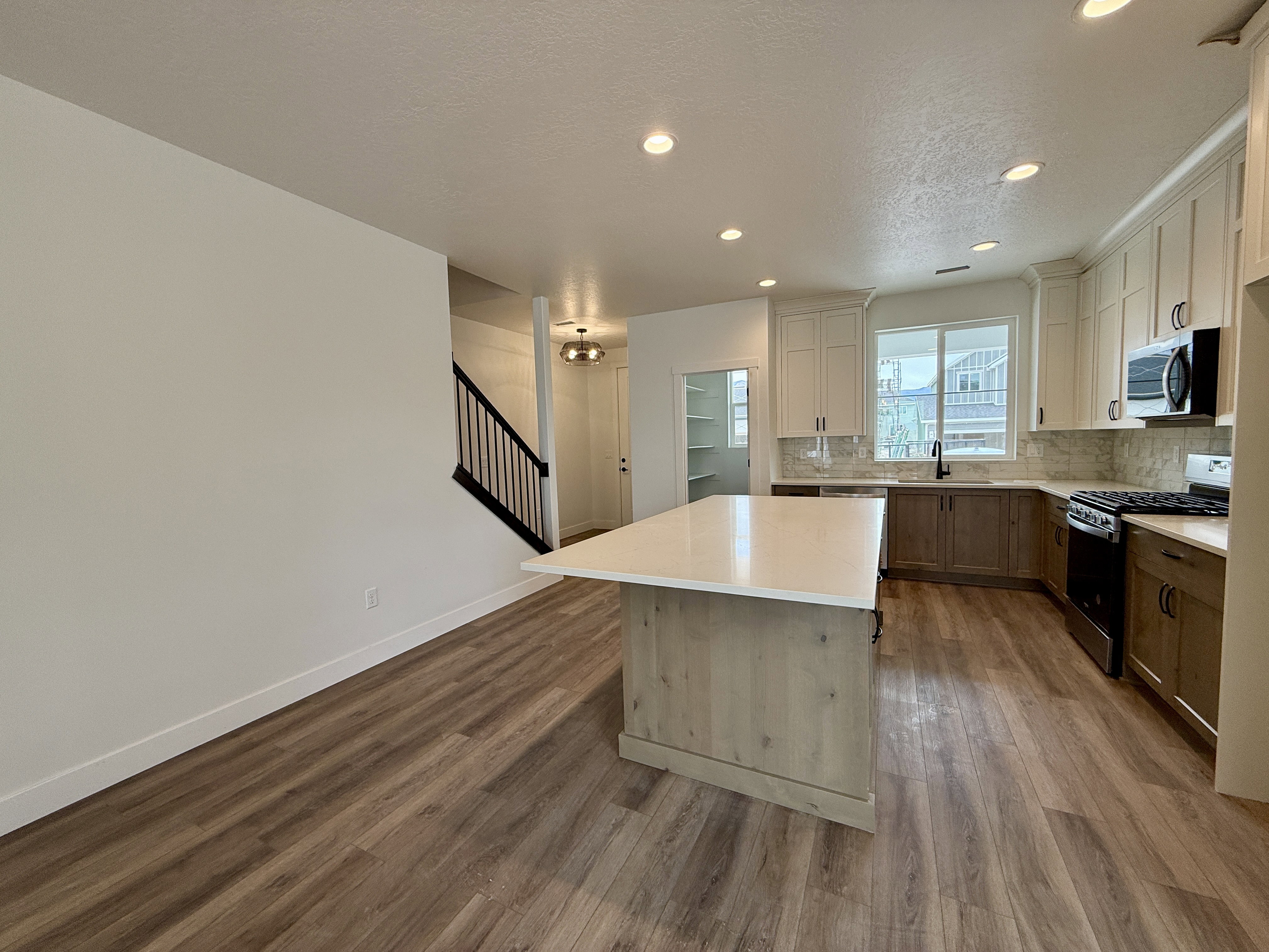 Kitchen featuring wood-finish flooring, a central island with a light-toned countertop, a two-tone cabinetry scheme, a built-in microwave, and recessed lighting