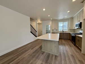Kitchen featuring wood-finish flooring, a central island with a light-toned countertop, a two-tone cabinetry scheme, a built-in microwave, and recessed lighting
