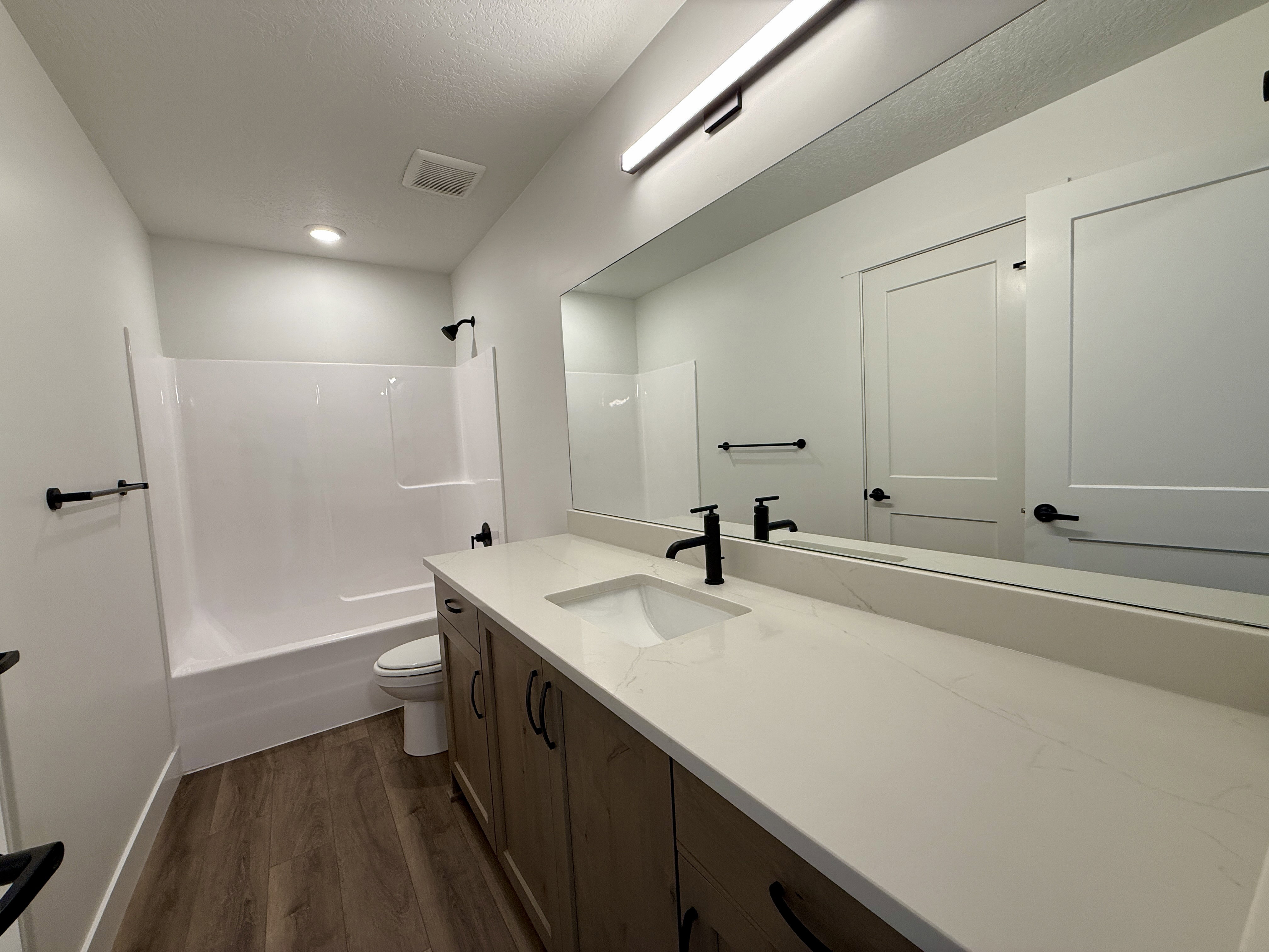 Bathroom featuring a wood-finish vanity with a single sink, light-toned countertop, and matte black fixtures