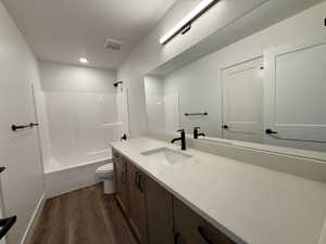 Bathroom featuring a wood-finish vanity with a single sink, light-toned countertop, and matte black fixtures