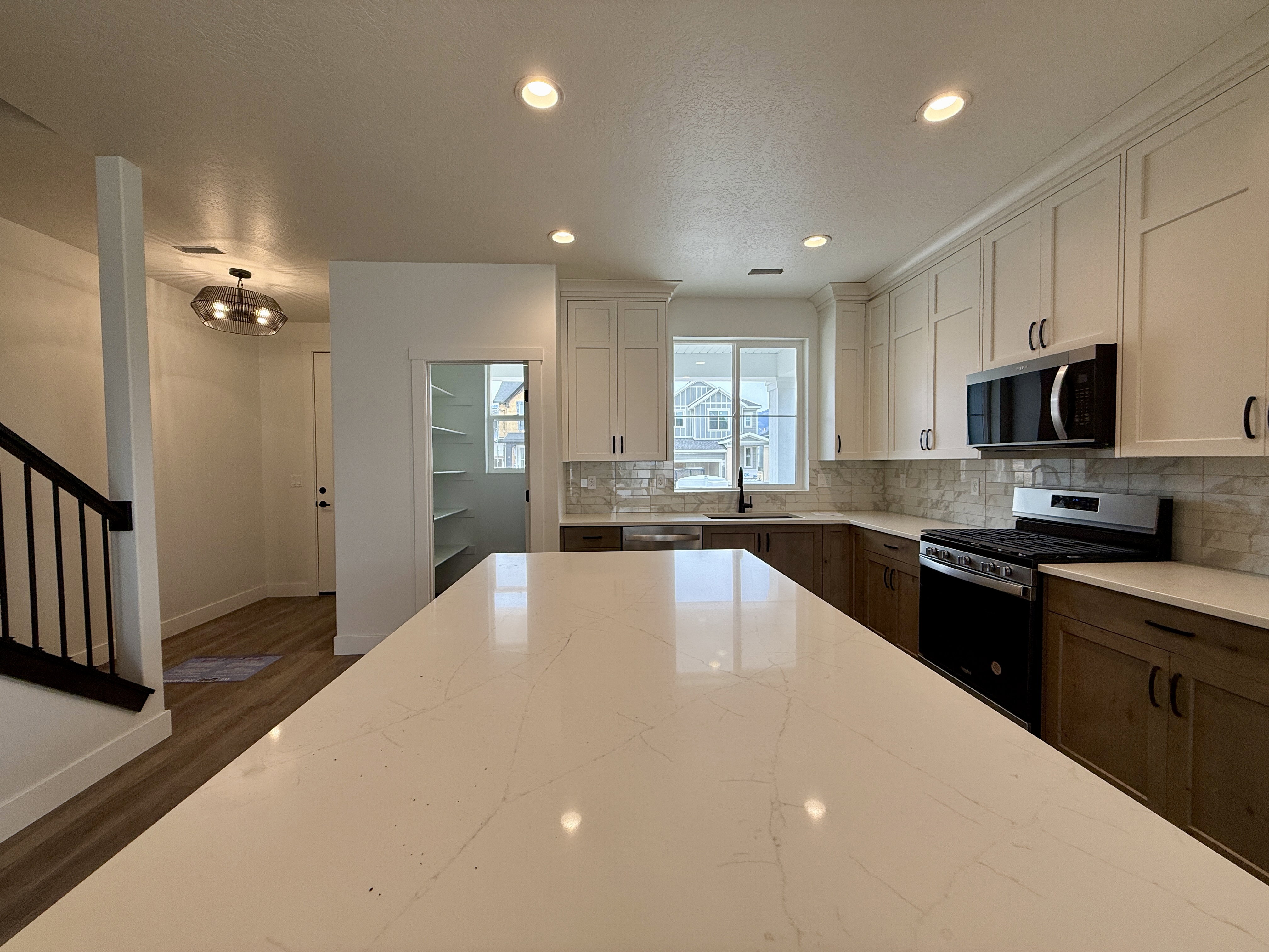 Spacious kitchen featuring a large island with a light-toned countertop, two-tone cabinetry, stainless steel appliances, and a tile backsplash