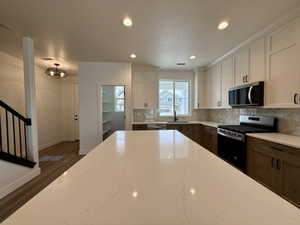 Spacious kitchen featuring a large island with a light-toned countertop, two-tone cabinetry, stainless steel appliances, and a tile backsplash