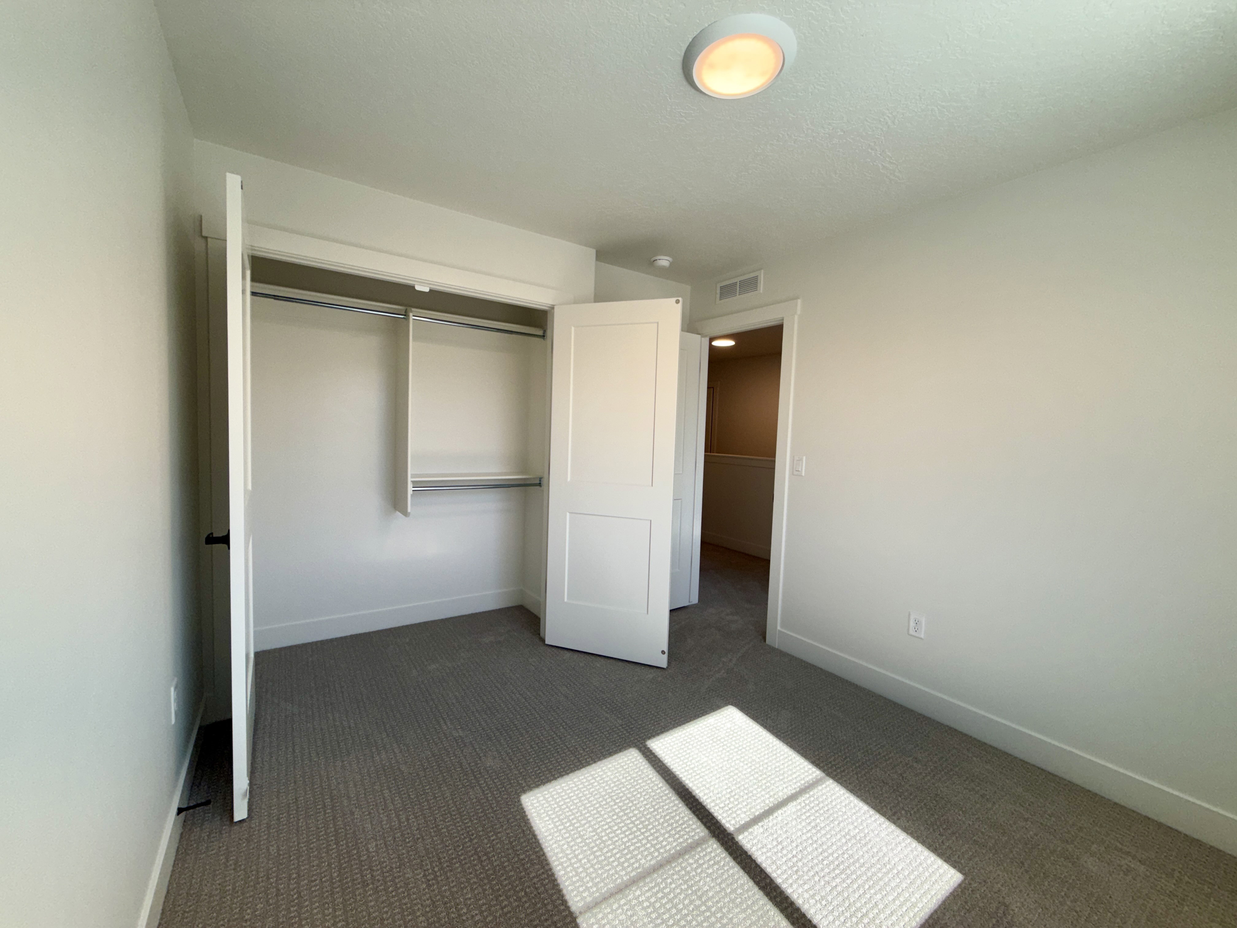 Neutral-toned room featuring a closet with bi-fold doors and shelving, carpeted flooring, and a flush-mount ceiling light