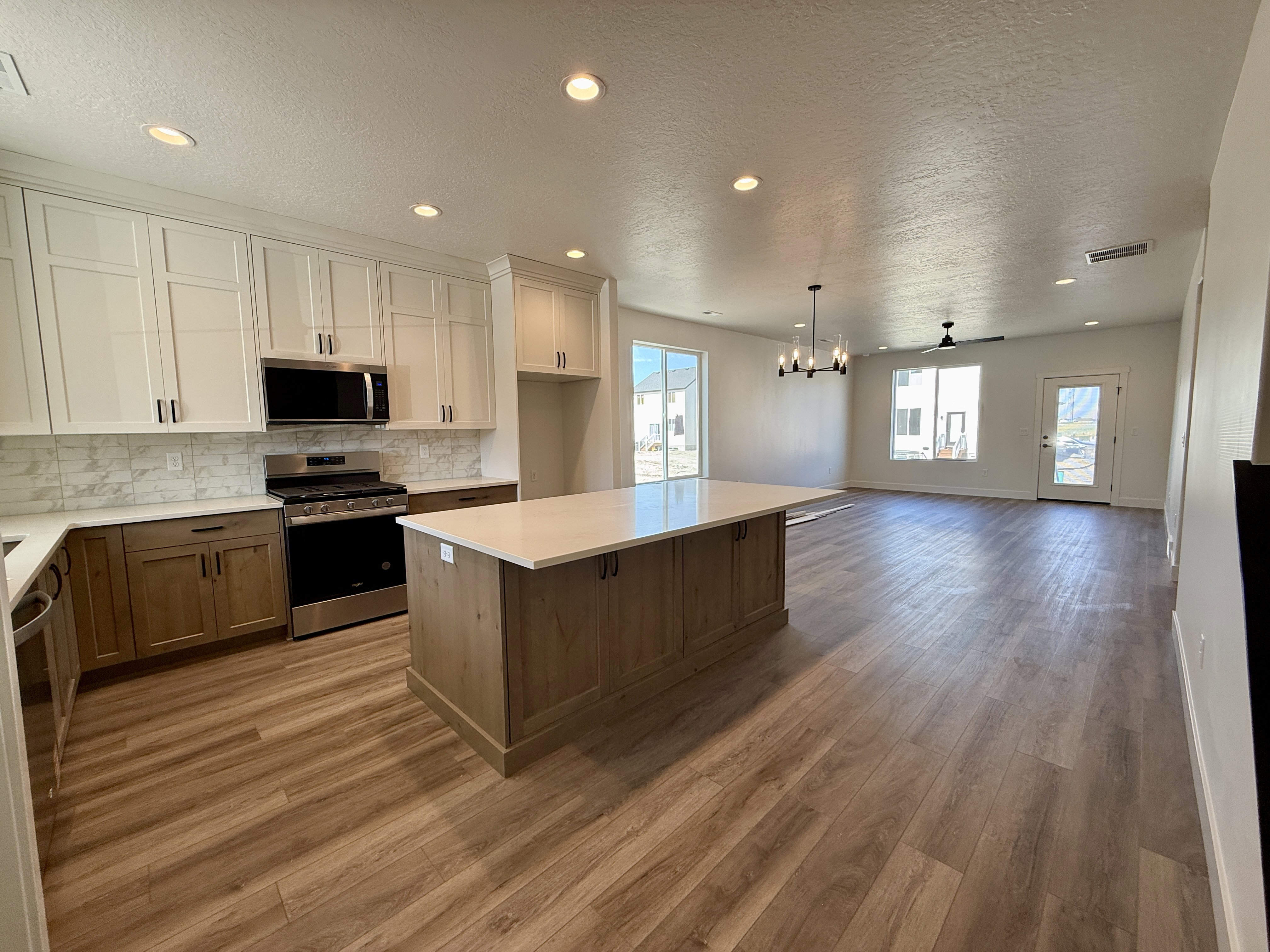 Open-concept kitchen featuring an island with a quartz-finish countertop, two-tone cabinetry, stainless steel appliances, and wood-finish flooring
