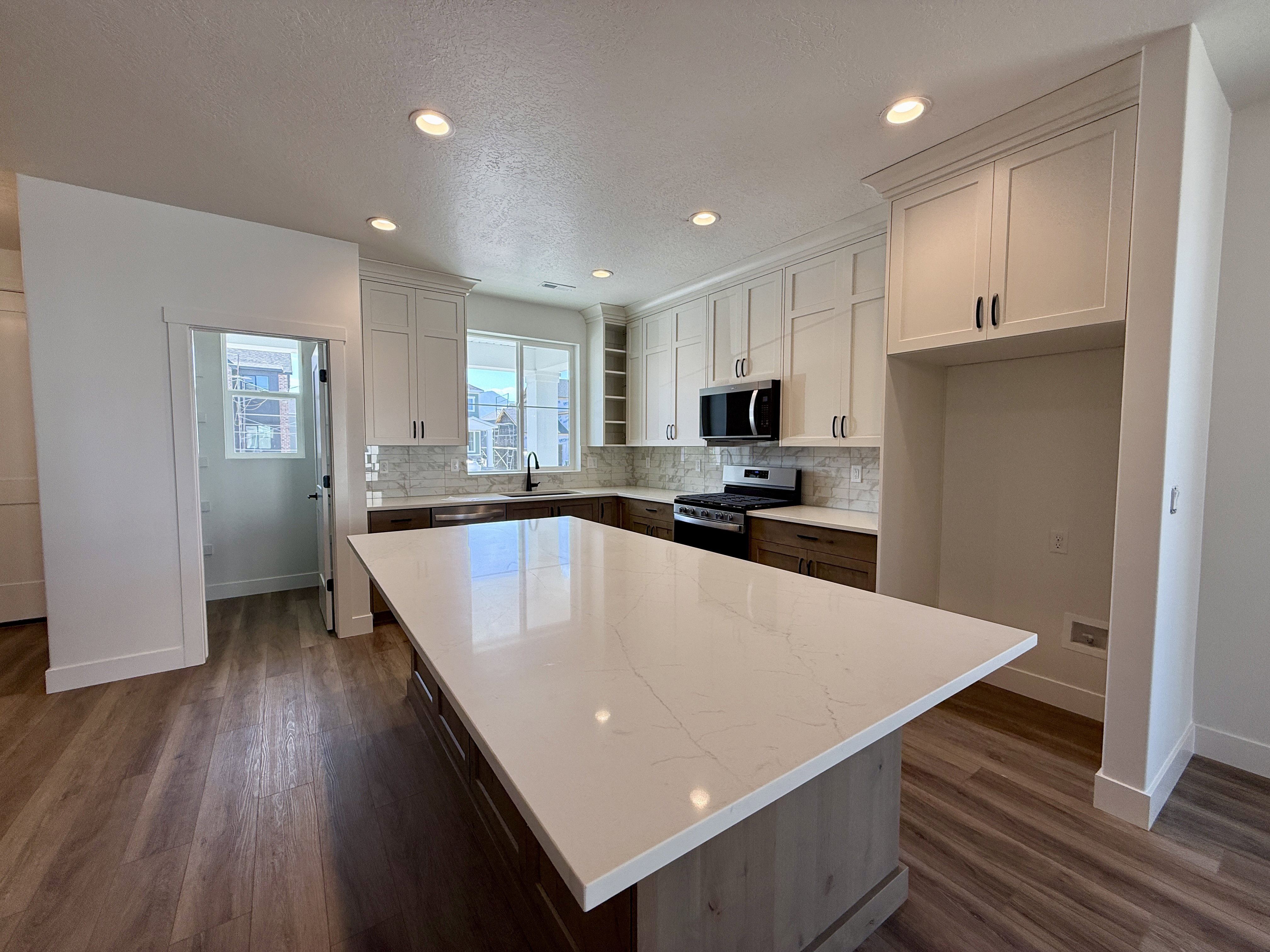 Kitchen featuring a large central island with a light-toned countertop, wood-finish flooring, white upper cabinetry, and dark lower cabinetry
