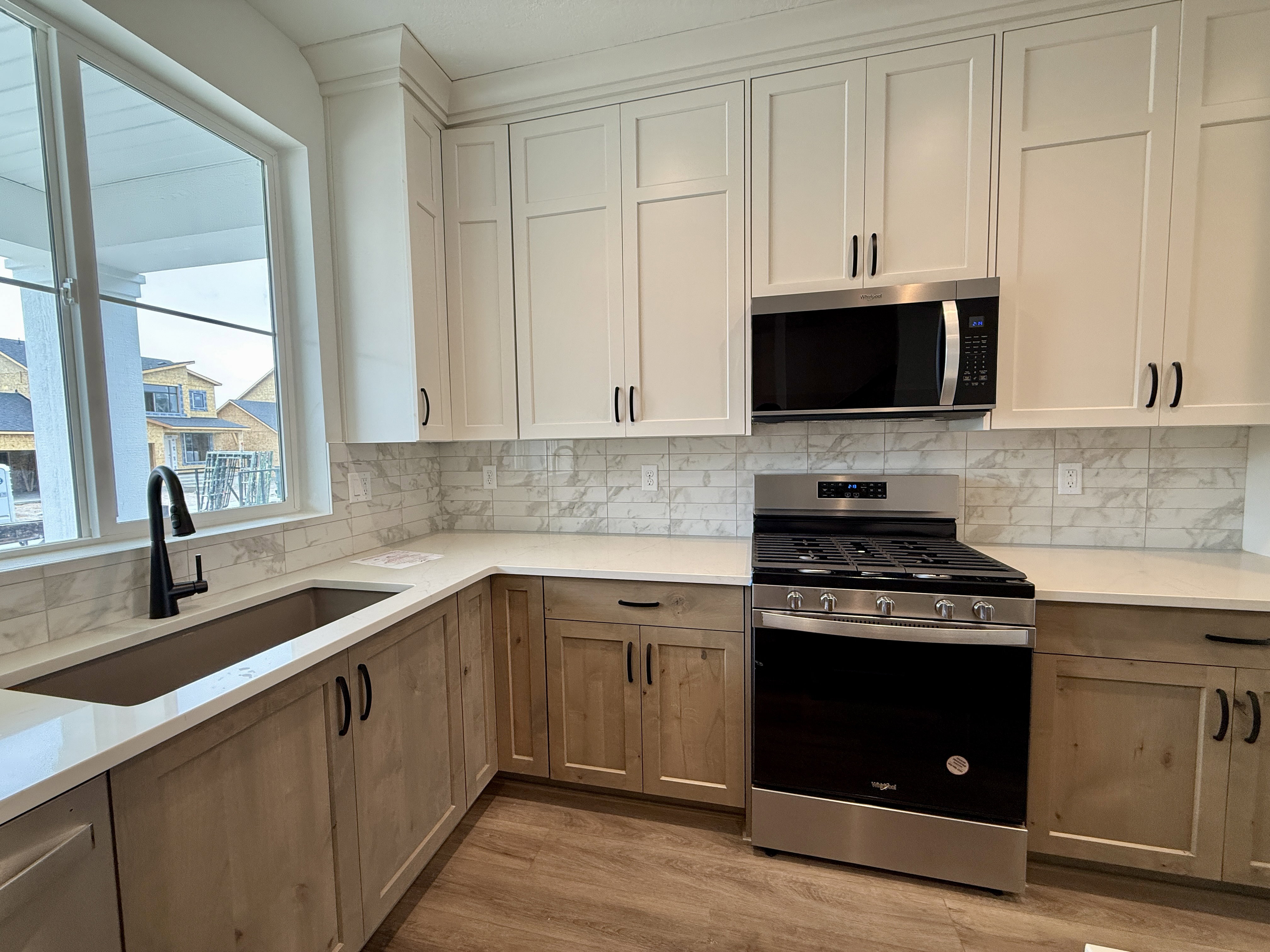 Modern kitchen featuring two-tone cabinetry with contrasting hardware, white quartz countertops, full subway tile backsplash, and stainless steel appliances