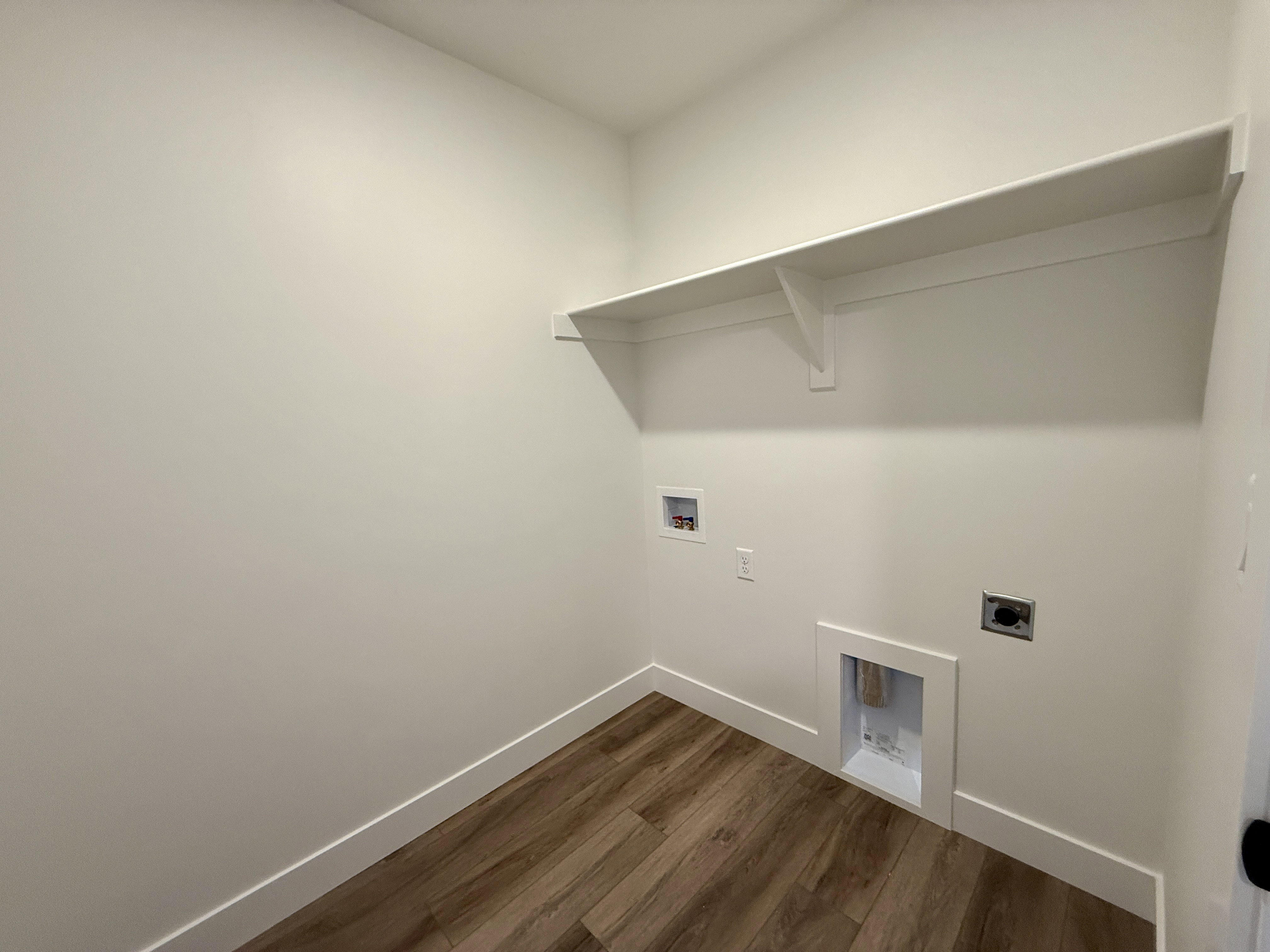 Utility area featuring wood-finish flooring, white walls, and a built-in storage shelf