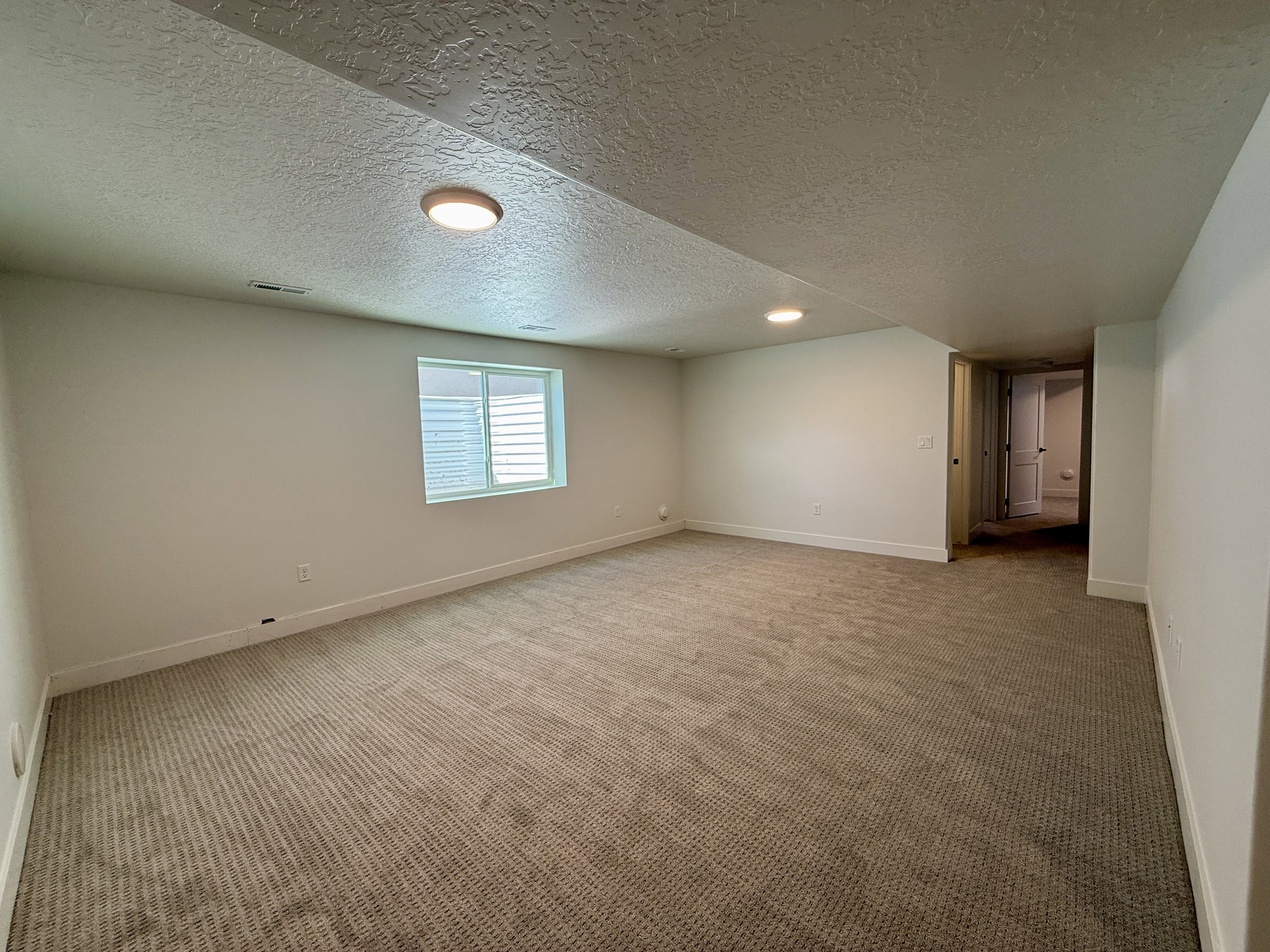 Spacious room featuring new carpet, fresh paint, a large egress window, recessed lighting, and a neutral color palette