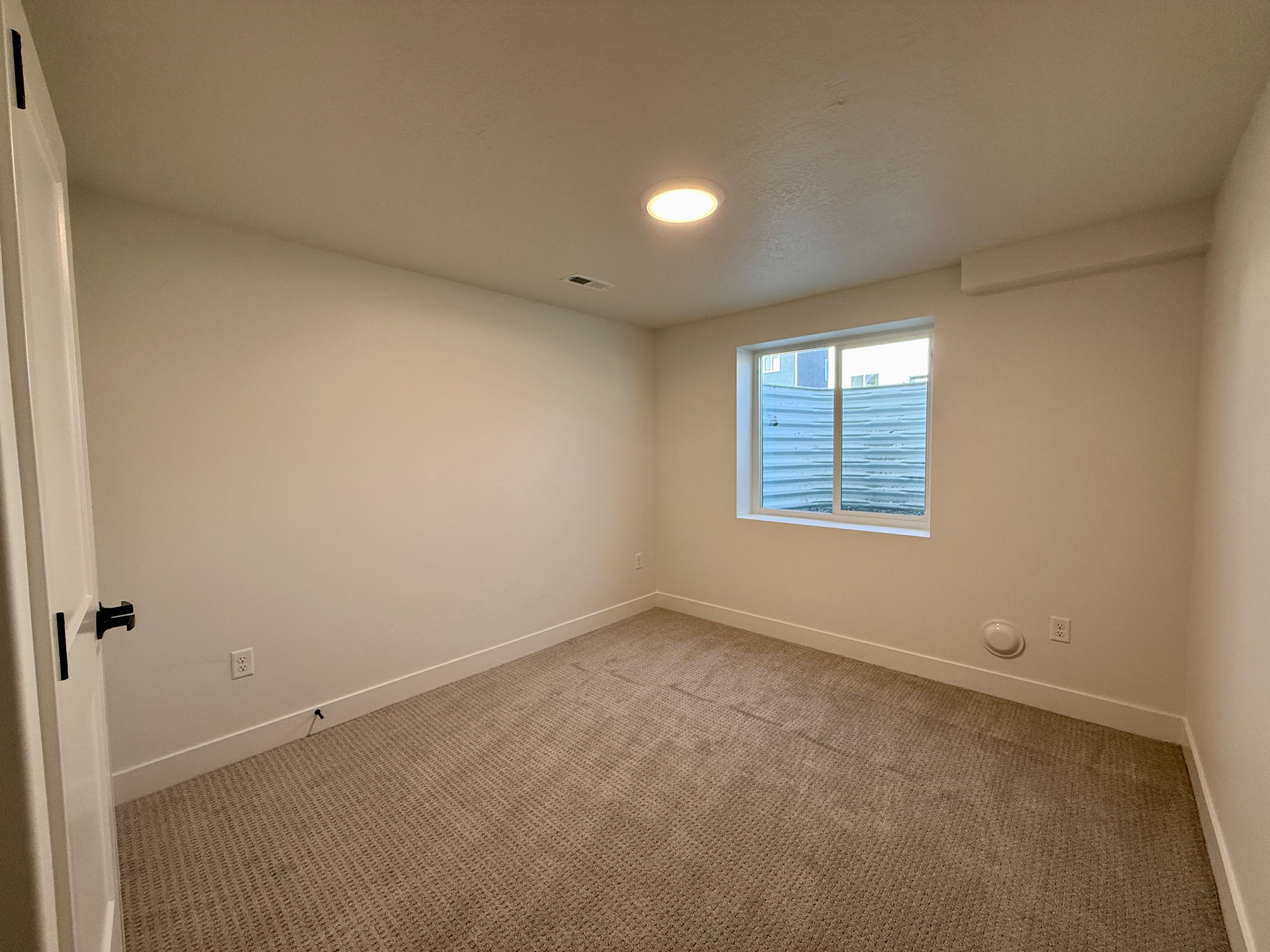 Bright interior room featuring a window, neutral-toned carpet, white baseboards, and a flush-mount ceiling light