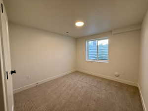 Bright interior room featuring a window, neutral-toned carpet, white baseboards, and a flush-mount ceiling light