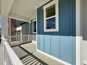Covered front porch featuring white railings, a concrete surface, and a beadboard ceiling