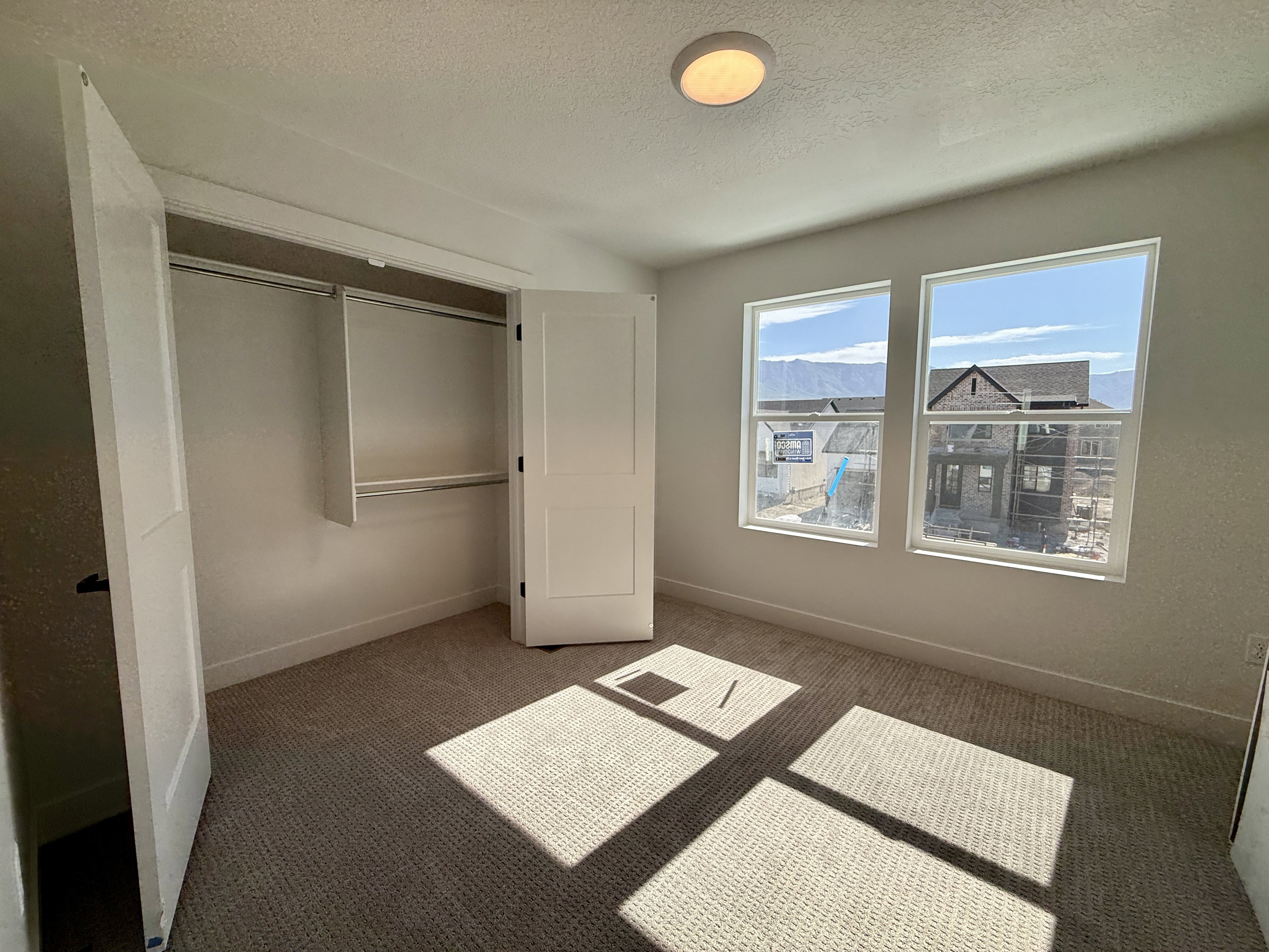 Carpeted room featuring two large windows, a built-in closet with double doors, and a ceiling-mounted light fixture