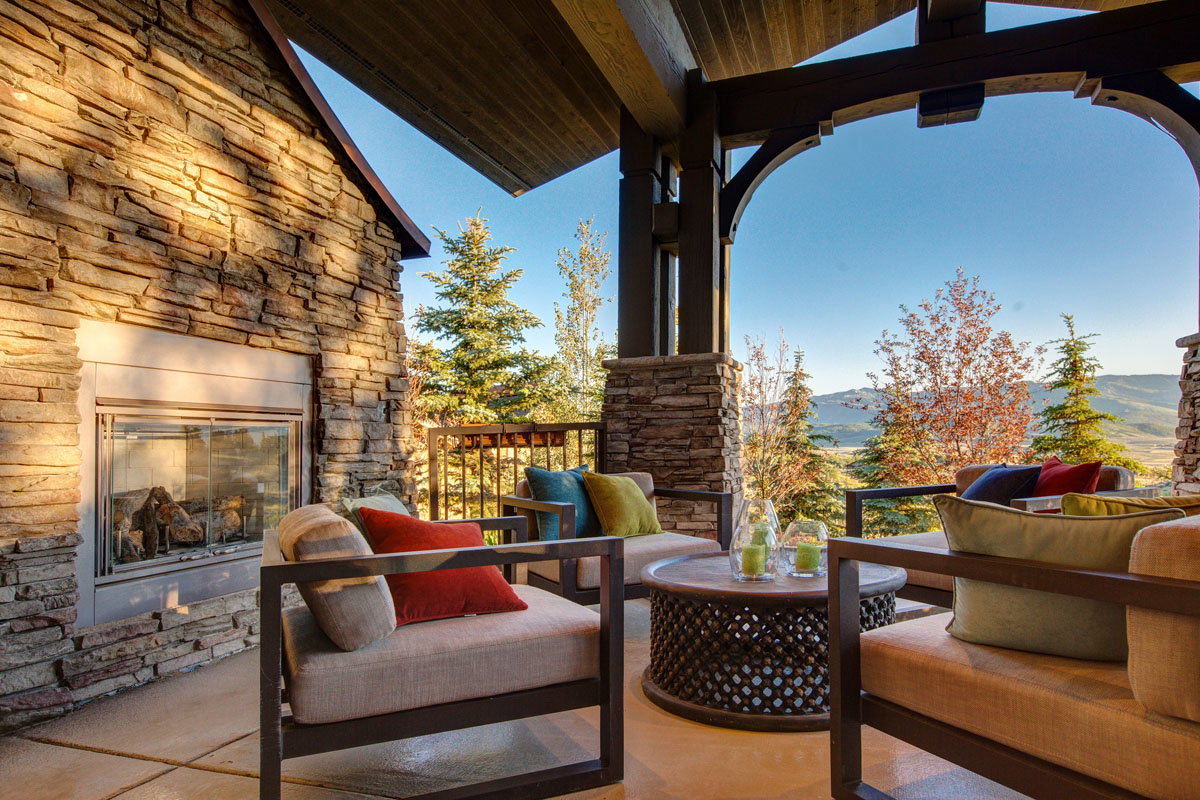 Covered outdoor patio featuring a stone-clad fireplace and wood-beamed ceiling
