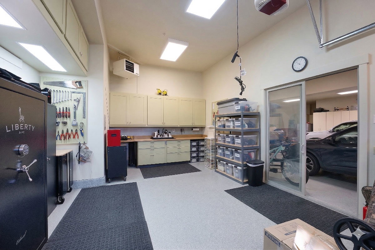 Spacious garage featuring extensive built-in cabinetry, durable epoxy-coated flooring, an integrated workbench with countertop space, fluorescent overhead lighting, and an additional sliding glass door leading to another garage bay