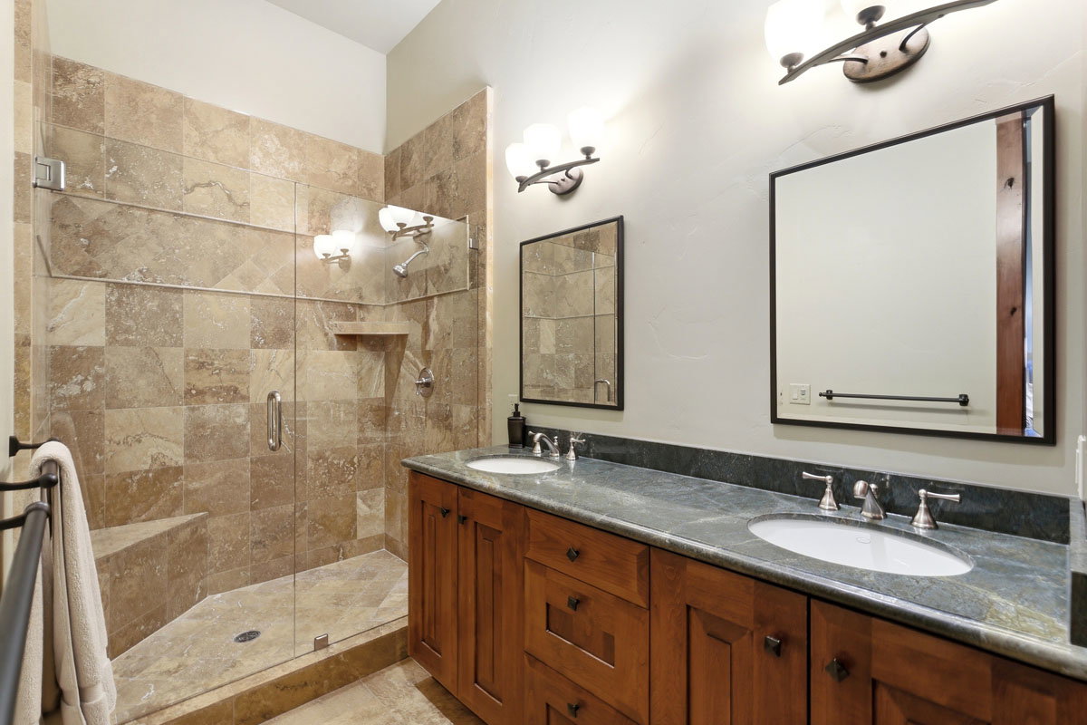 Spacious bathroom featuring a glass-enclosed shower with stone tile surround and built-in bench