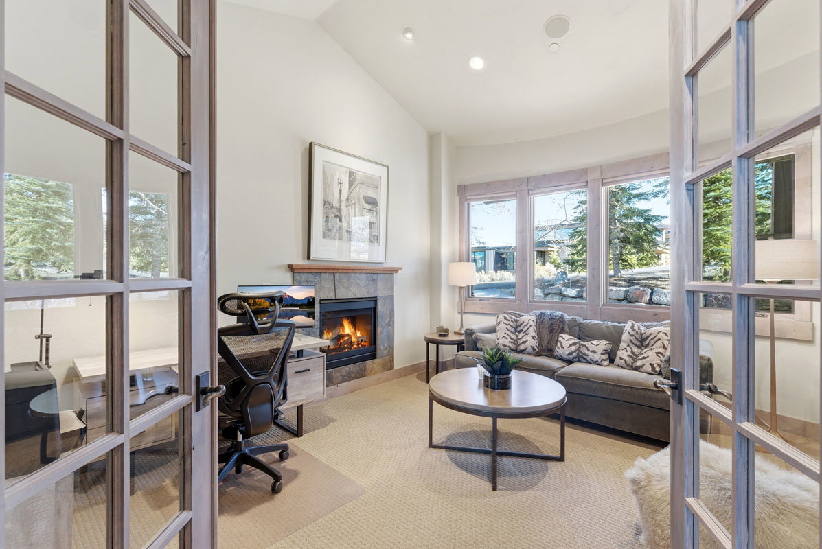 Room featuring double French doors with grid-patterned glass, a stone-clad fireplace with a wood mantel, a curved wall of large windows, recessed ceiling lighting, and light-toned carpeting