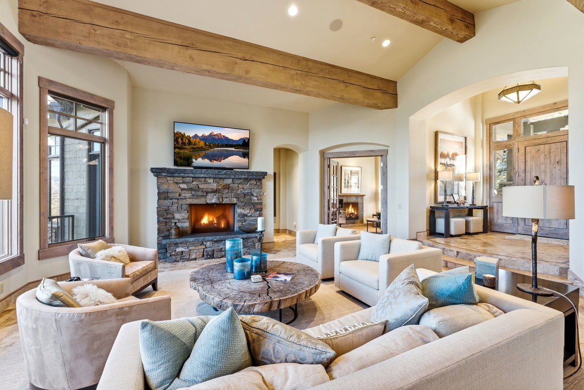 Spacious living area featuring exposed wood ceiling beams, a stone-faced fireplace, and high vaulted ceilings