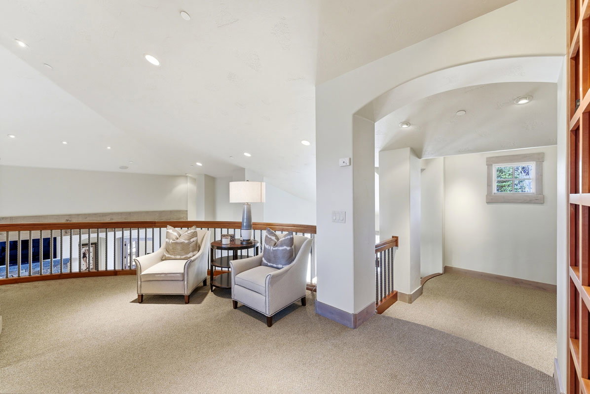 Open loft area featuring recessed lighting, a wood and iron railing, an arched entryway, and a window with wood trim