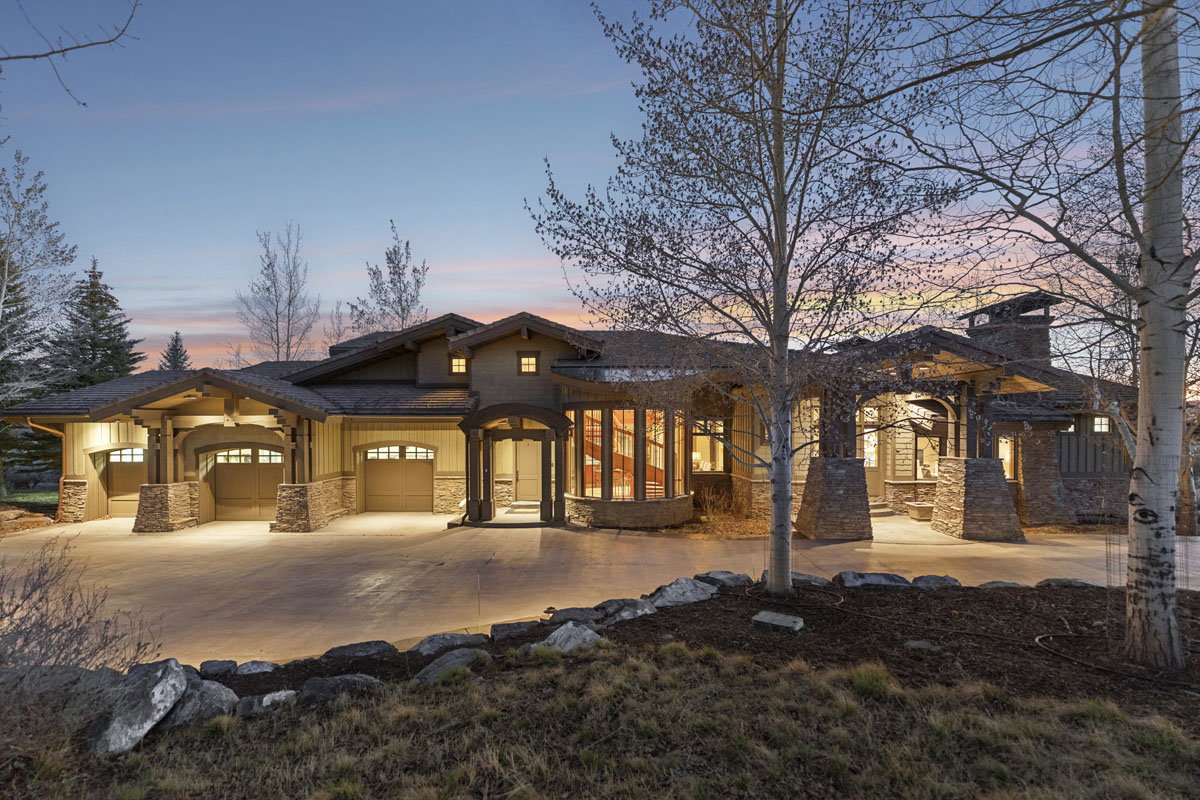 Expansive Craftsman-style residence featuring a stone and stucco exterior, multiple attached garages, a porte-cochère, and a stone chimney