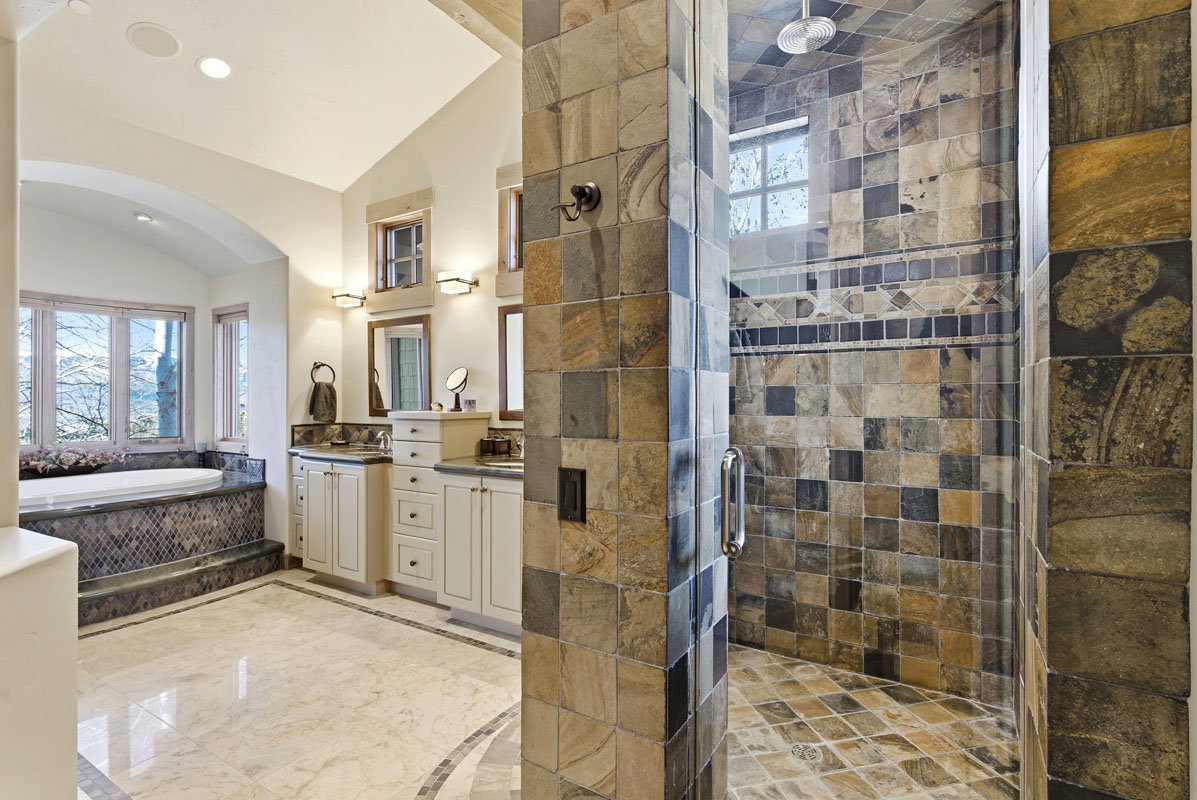 Stone-tiled walk-in shower with glass enclosure and overhead shower fixture