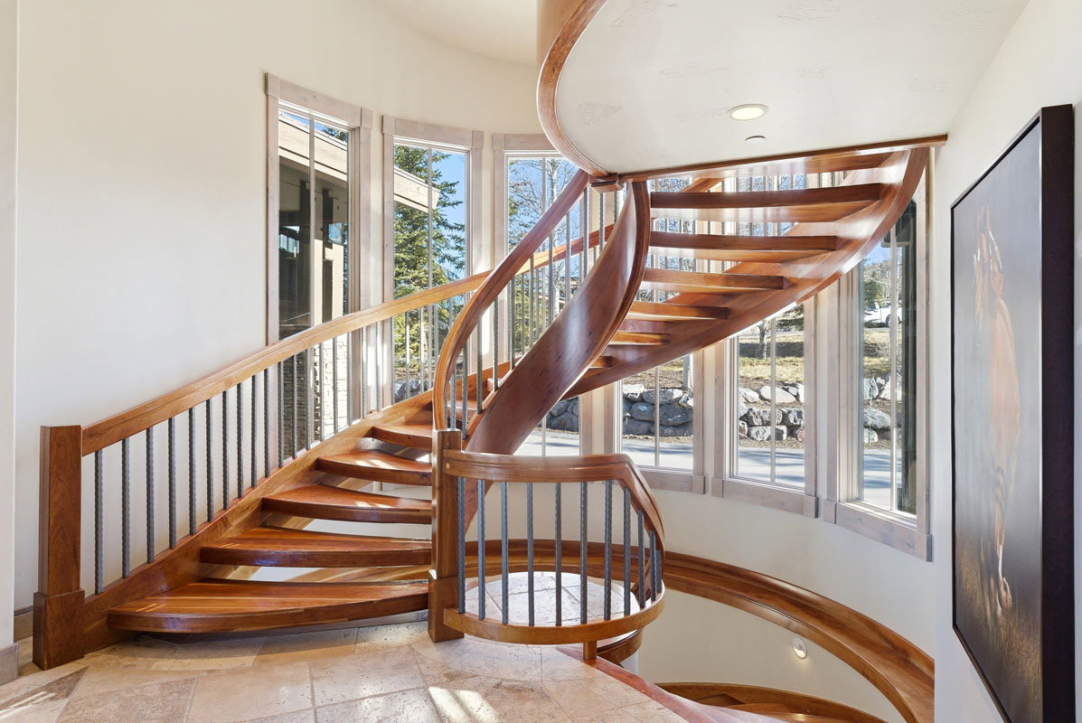 Curved wood staircase with wrought iron balusters, natural light from multiple windows, and recessed ceiling lighting