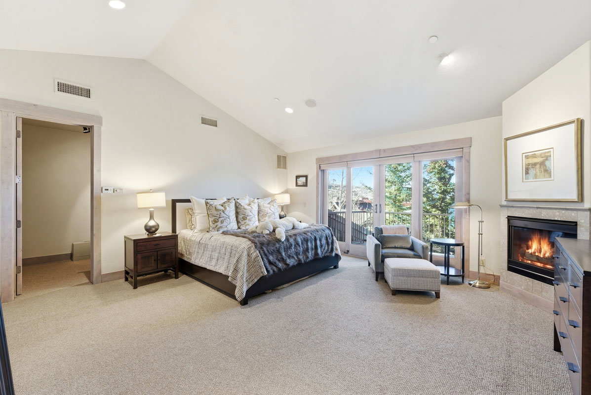 Spacious room featuring vaulted ceilings, a built-in fireplace with stone surround, a large glass sliding door opening to a private balcony, and light-colored carpet flooring