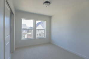 Light gray walls complement the neutral carpeting in this room featuring two large windows, a flush-mount ceiling light fixture, and a two-panel sliding closet door