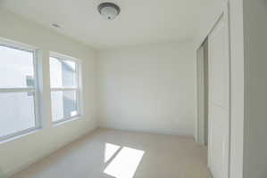 Room with light neutral wall paint, two large windows, neutral carpet flooring, and a sliding closet door
