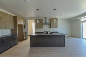 Open-concept kitchen featuring an island with an undermount sink, pendant lighting, stainless steel appliances, and wood-finish flooring