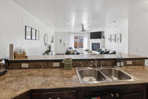 Kitchen peninsula featuring a double basin stainless steel sink with a chrome faucet, speckled countertops, and dark wood-finish cabinetry